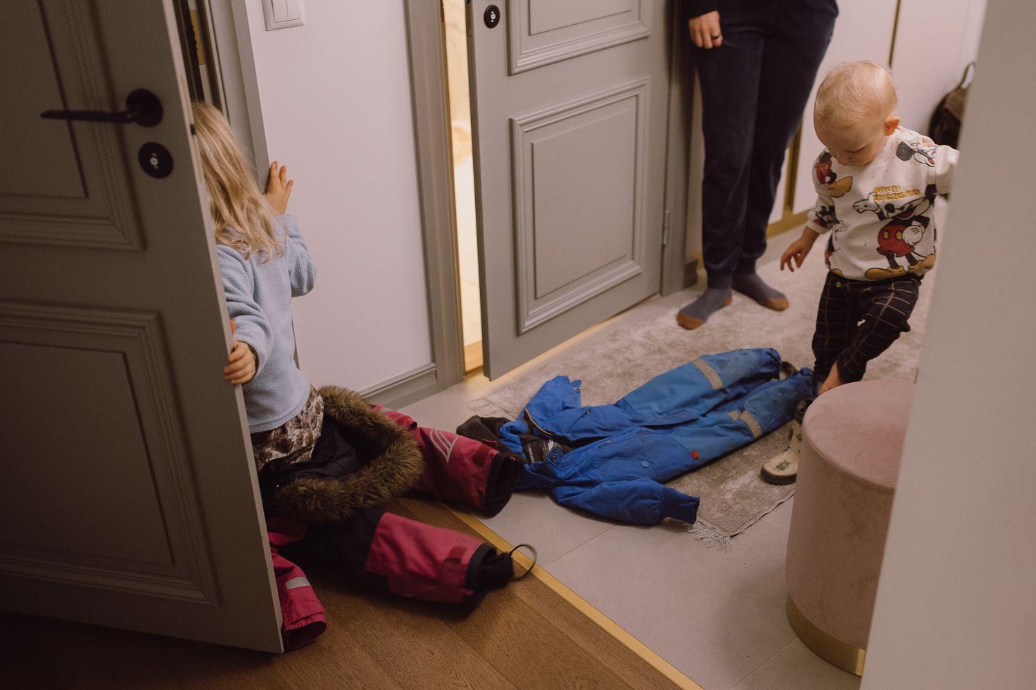 Parents helping young child get ready in bedroom with white crib and scattered clothing.