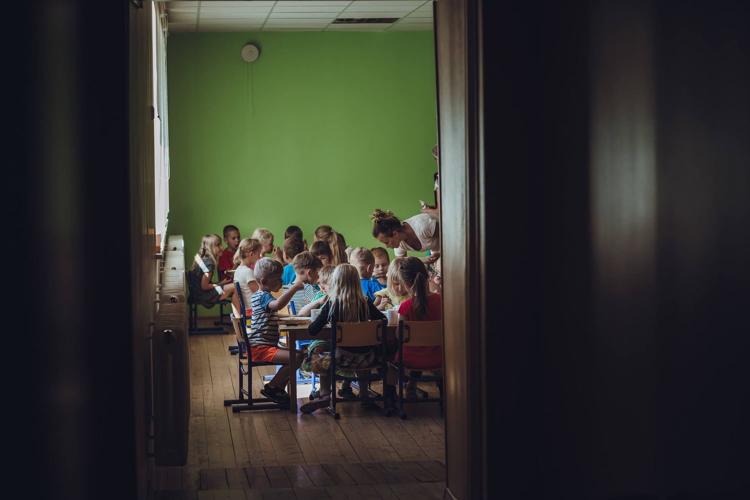 View through doorway of students sitting in classroom with bright green walls during lesson.