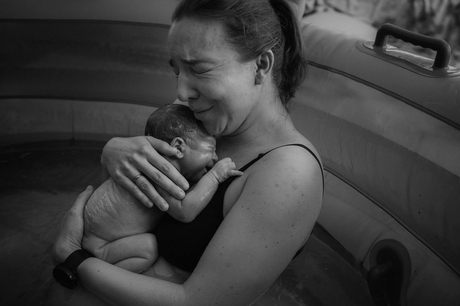 Emotional moment captured in black and white as a newborn is cradled in a birthing pool.