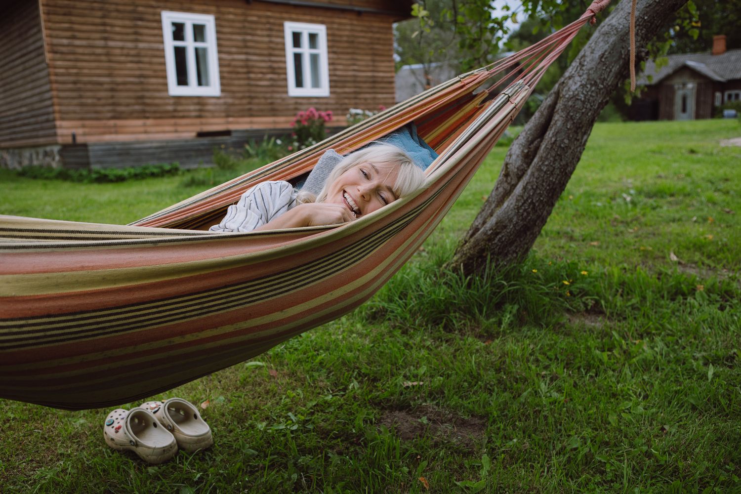 Person relaxing in brown hammock outside traditional wooden countryside house.