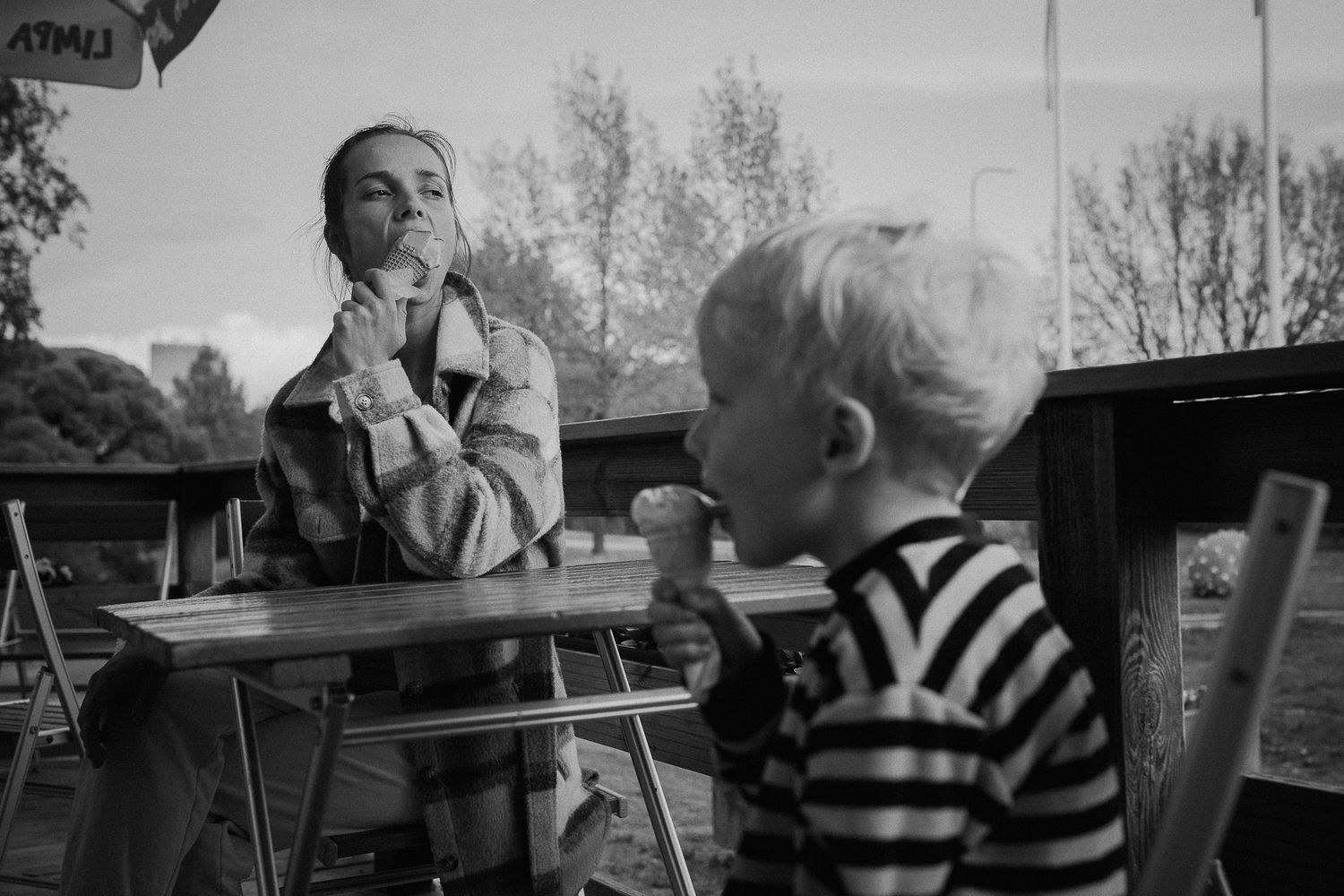 A vintage black and white photo of a child in a striped shirt sitting at an outdoor table.