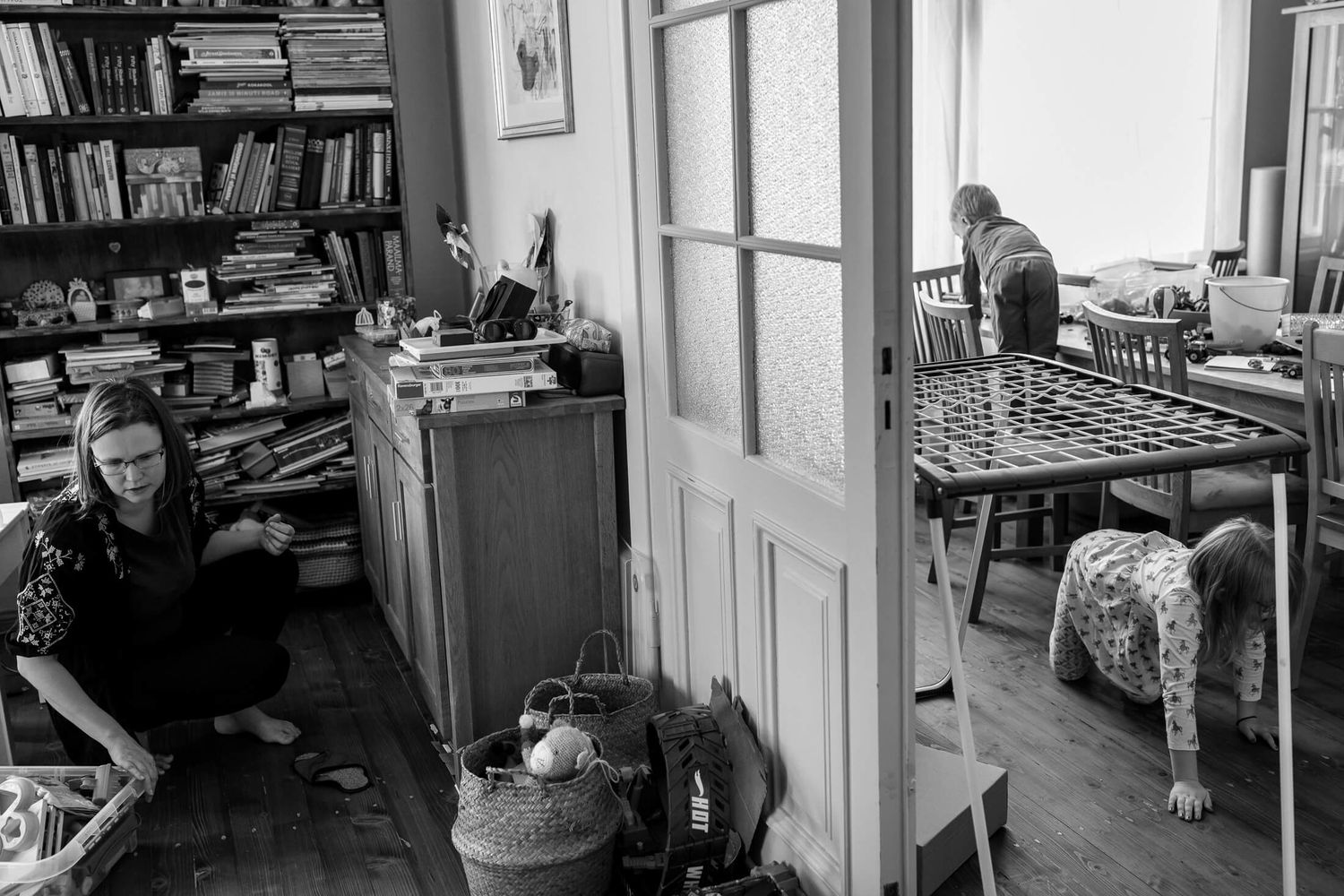 Black and white photo of interior room with bookshelves and people in separate spaces.