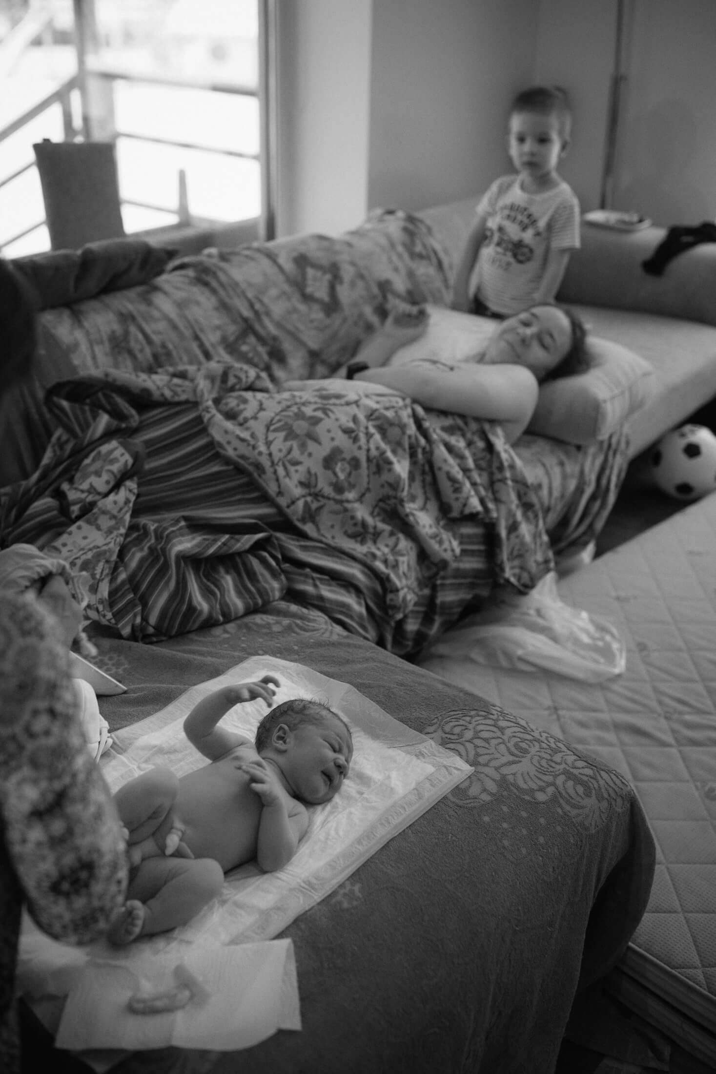Black and white photo of someone sleeping peacefully in bed with patterned blankets.