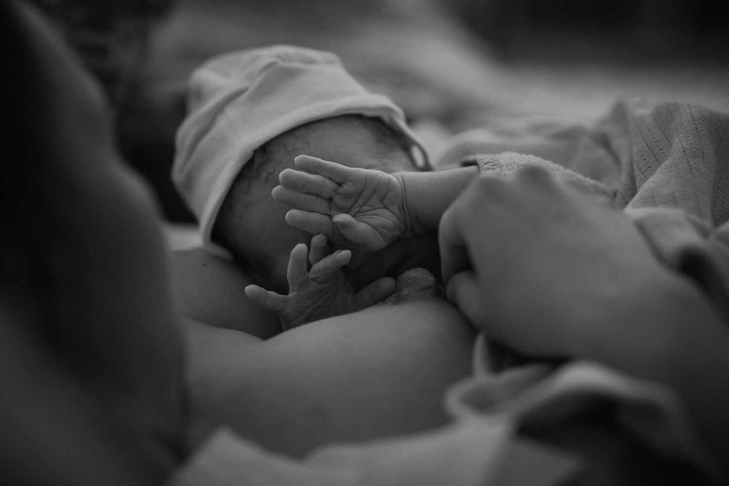 Close-up black and white image of gentle hands supporting a newborn.