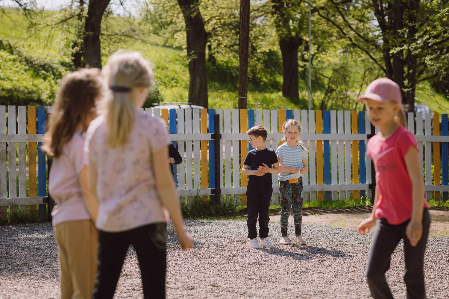 Children playing together in an outdoor playground area near a white fence.