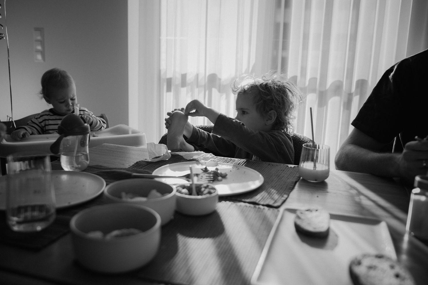 Black and white photo of young children eating at a dining table with plates and glasses nearby.