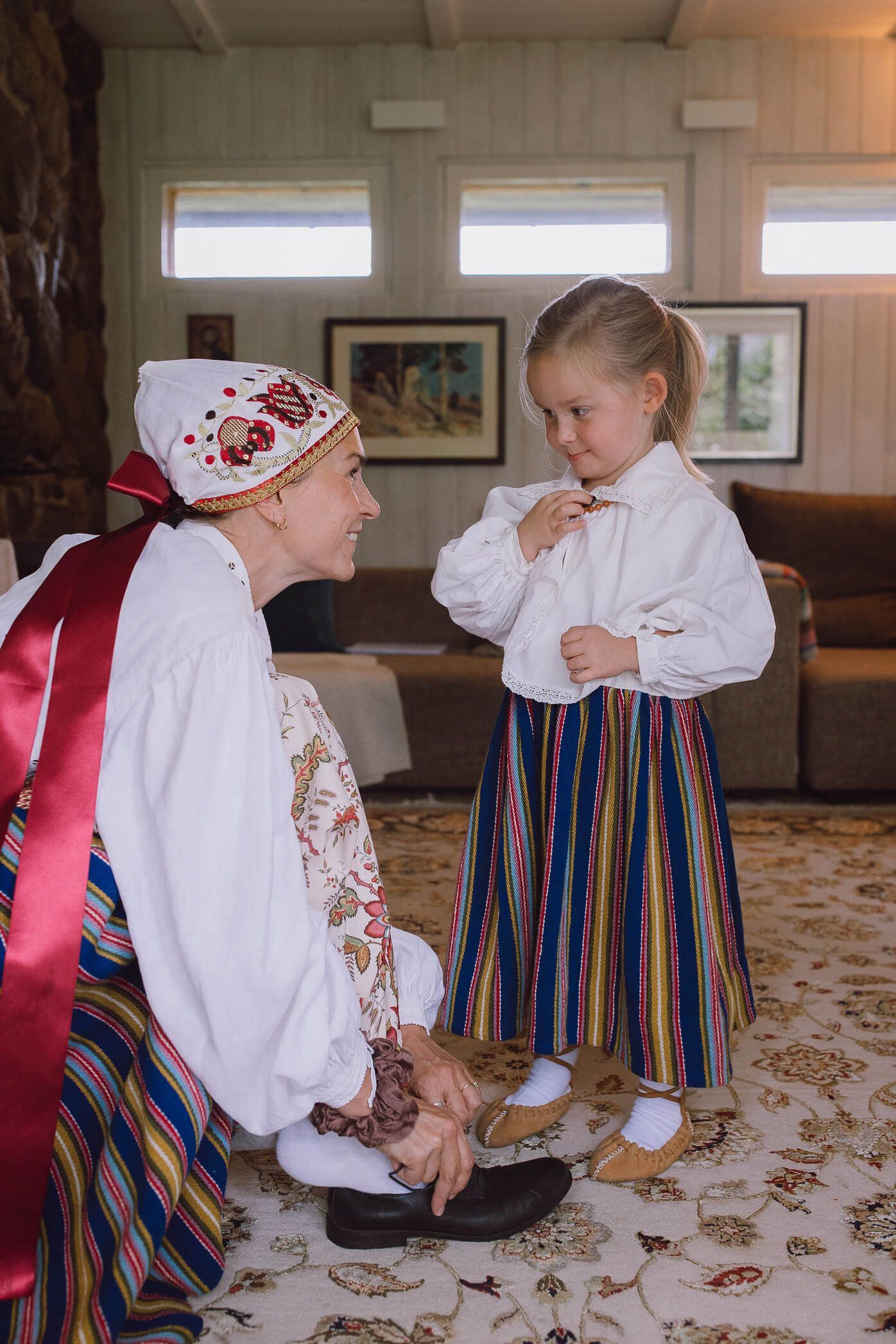 Woman and young girl wearing traditional Nordic folk costumes indoors, sharing a warm moment together.
