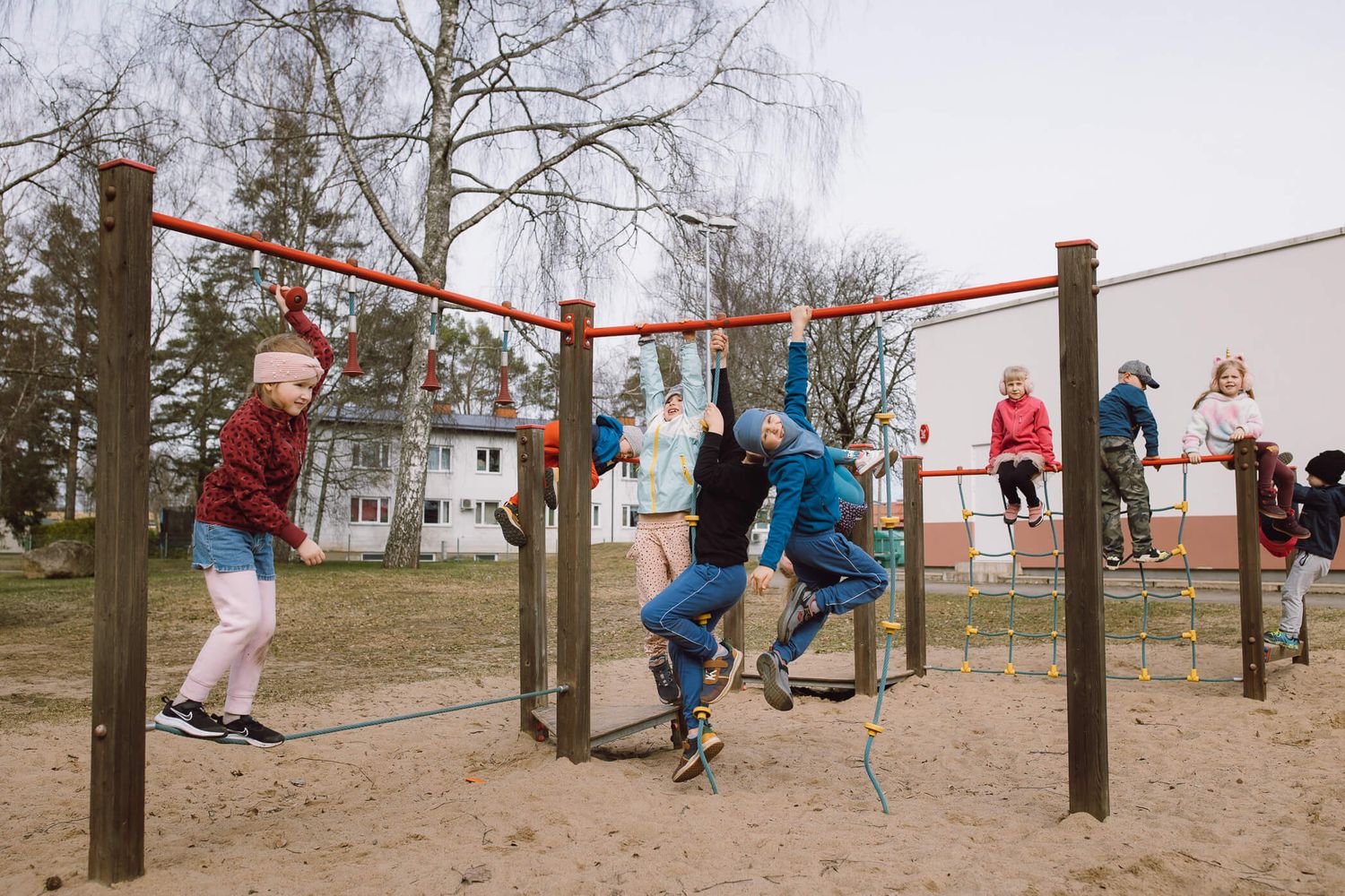 Children play and climb on outdoor playground equipment with metal bars and poles on a cloudy day.