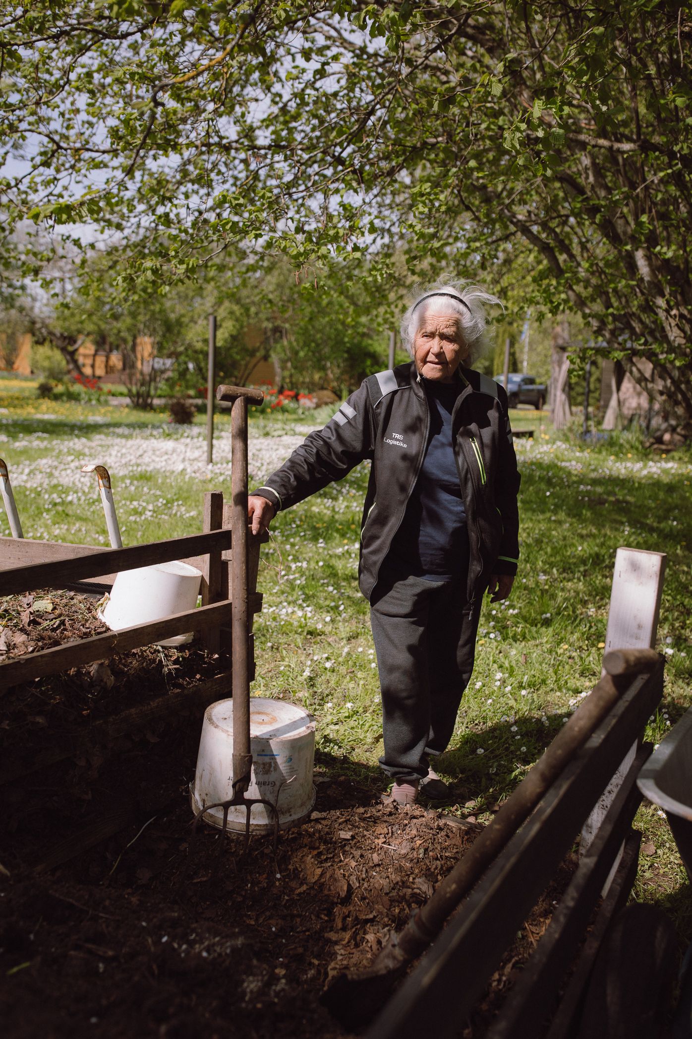 A person wearing dark clothing works in a raised garden bed, preparing soil for planting in a sunny outdoor setting.
