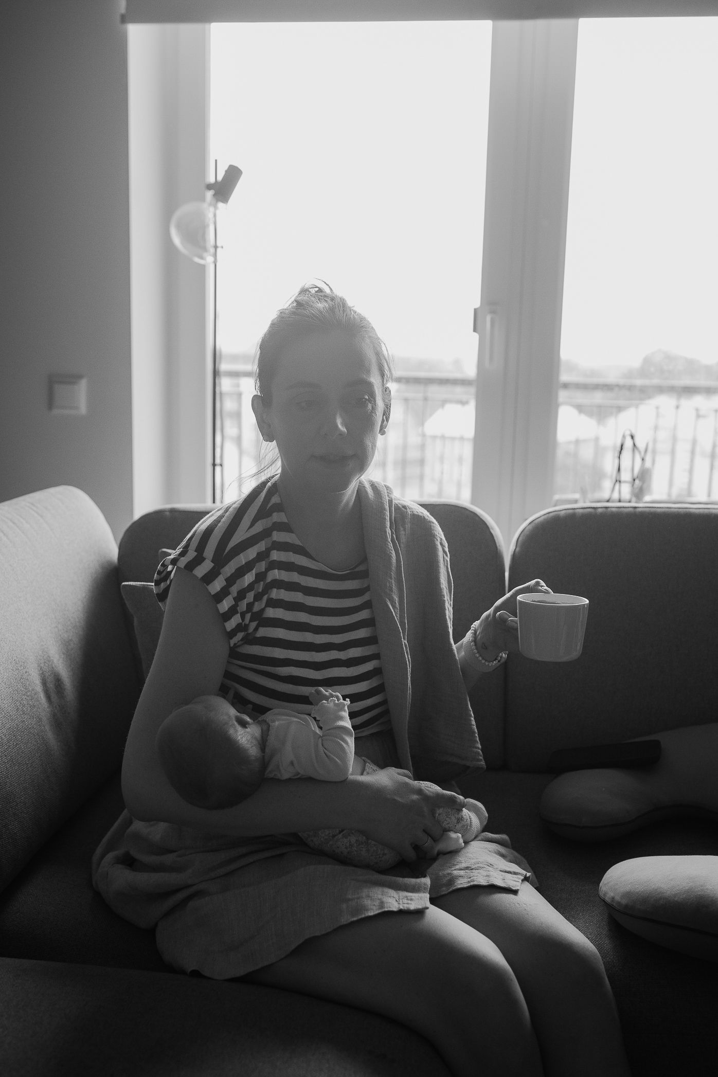 Person in striped shirt relaxing on couch by bright windows.
