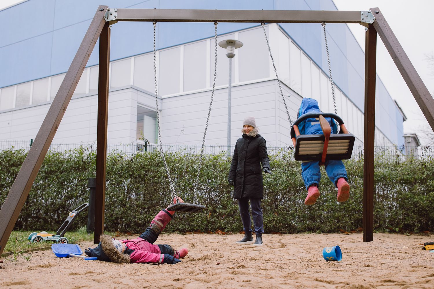 Children's playground with wooden swing set against a white building exterior.