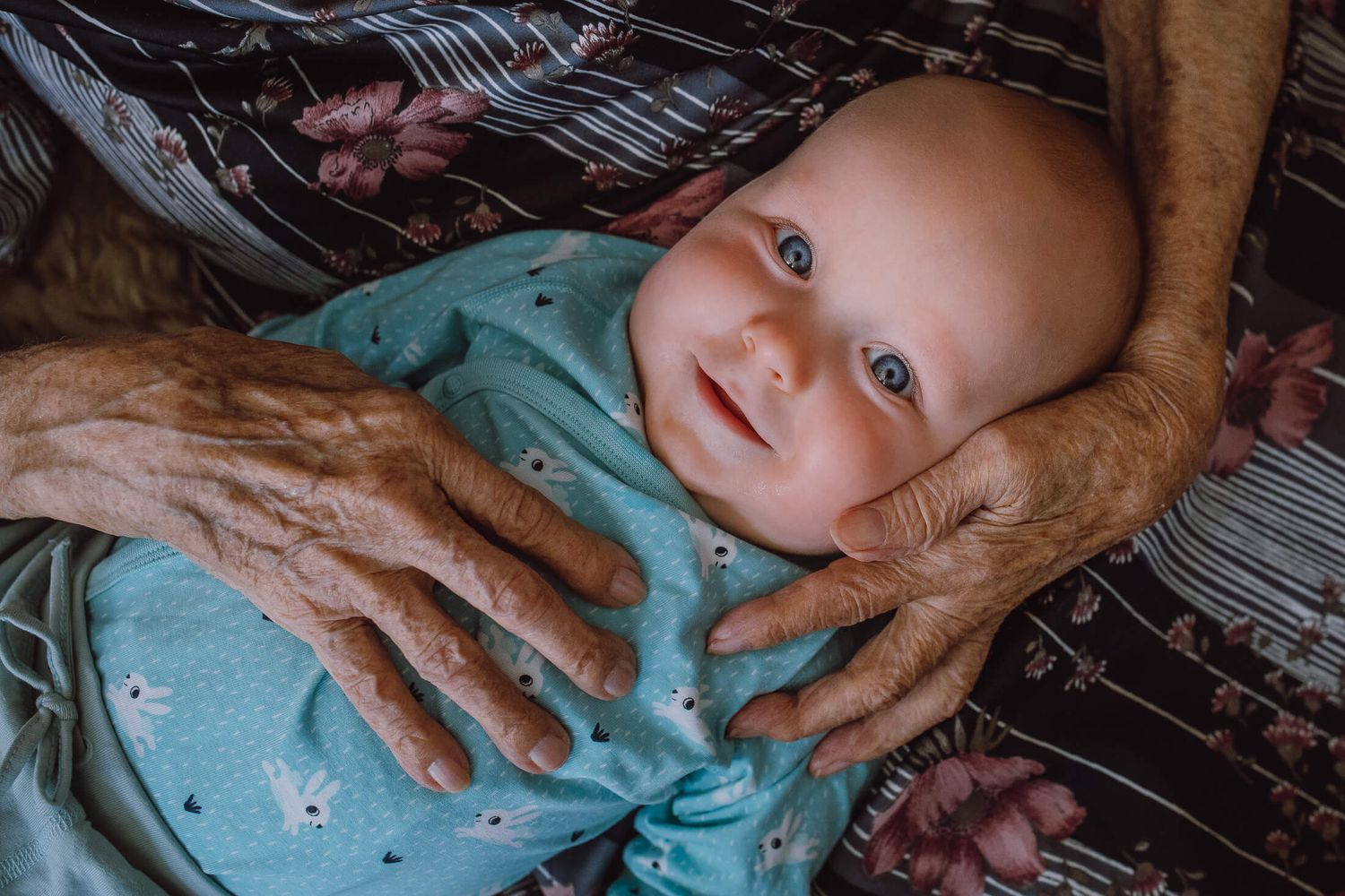 Gentle hands touching a baby wearing a turquoise outfit on a patterned surface.