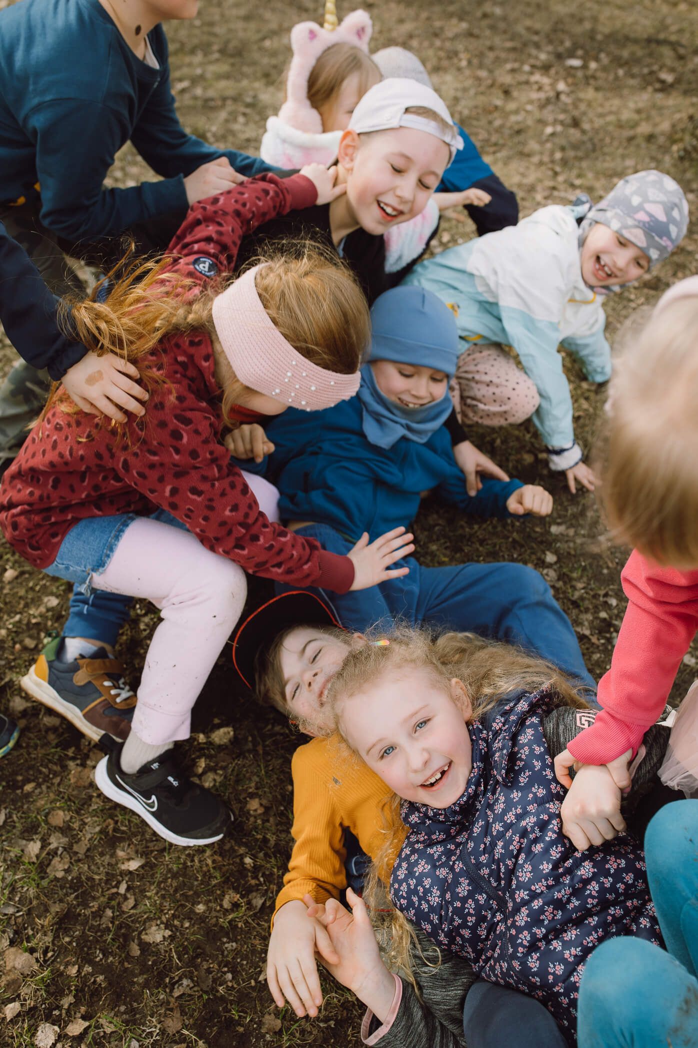 A group of children playing and laughing together while lying on the ground outdoors.
