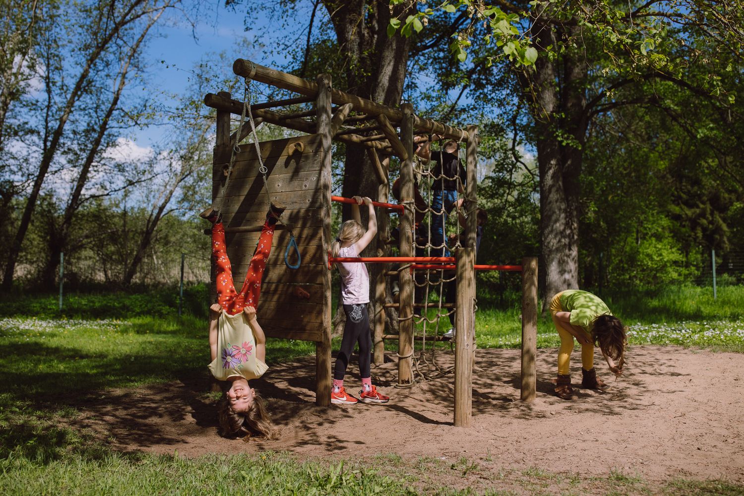 Children playing on wooden playground equipment in a natural wooded setting.