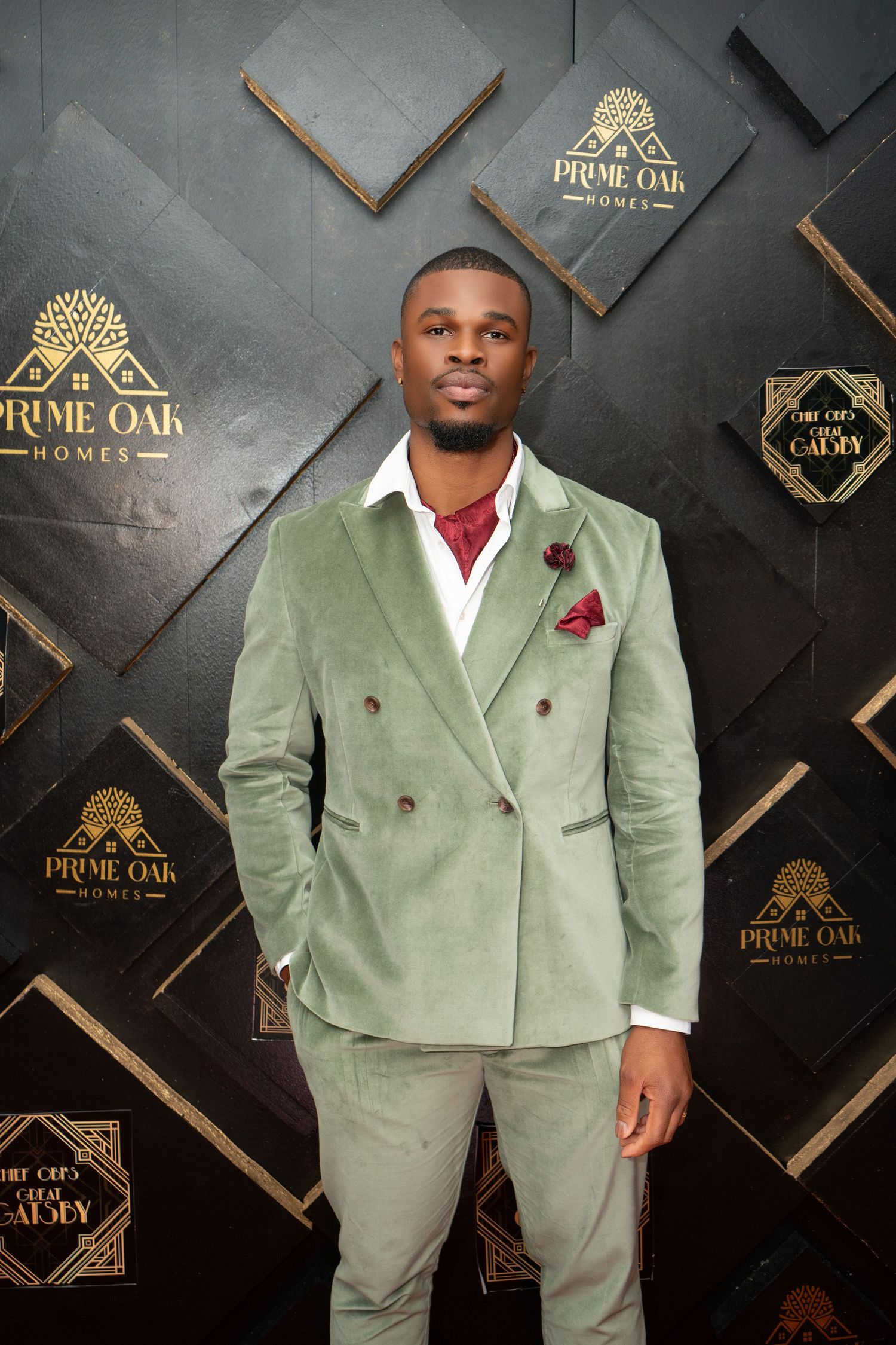 A mint green double-breasted suit with white shirt and red boutonniere against a dark geometric backdrop.