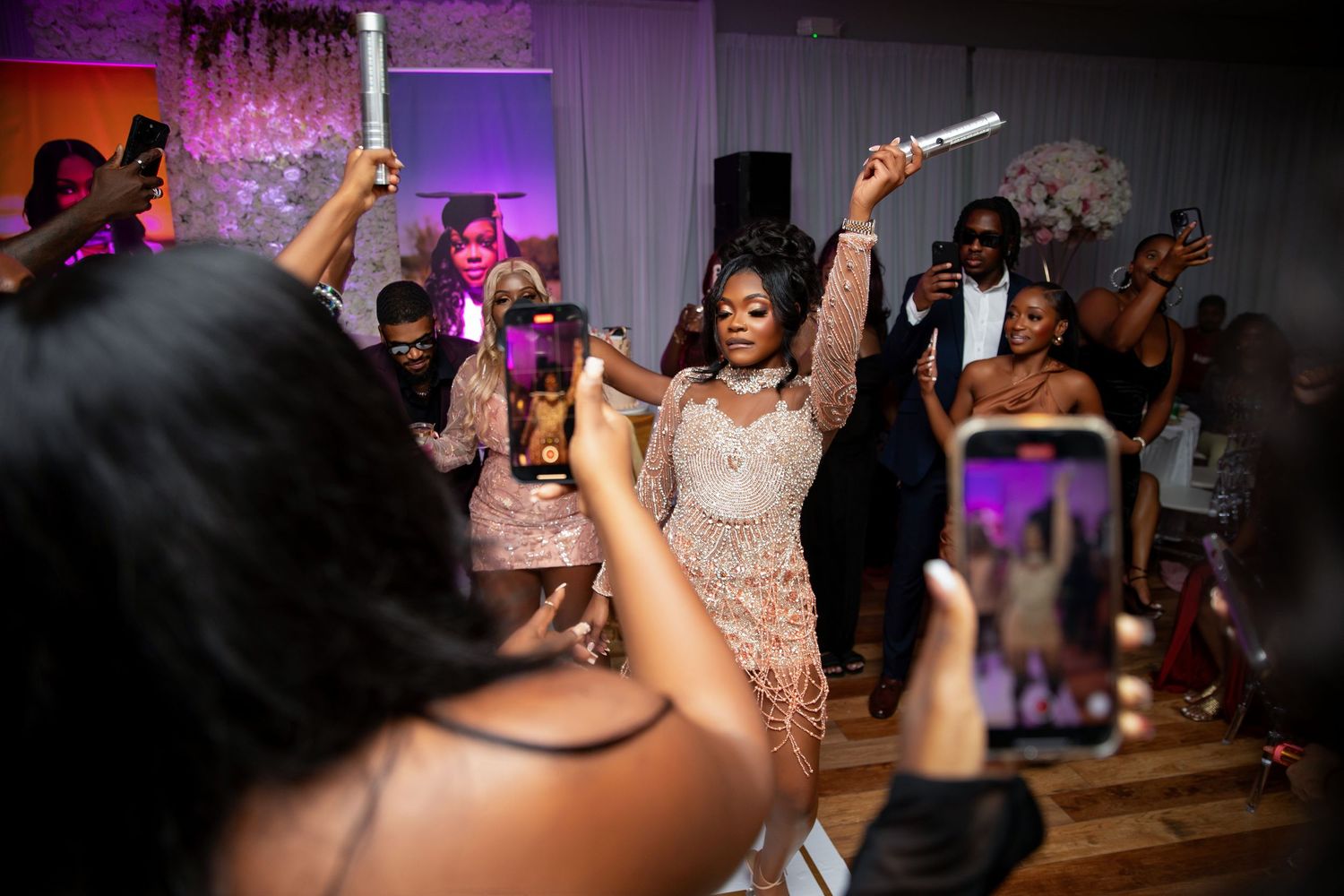 People dance and celebrate at a wedding reception with colorful purple lighting and a festive atmosphere.