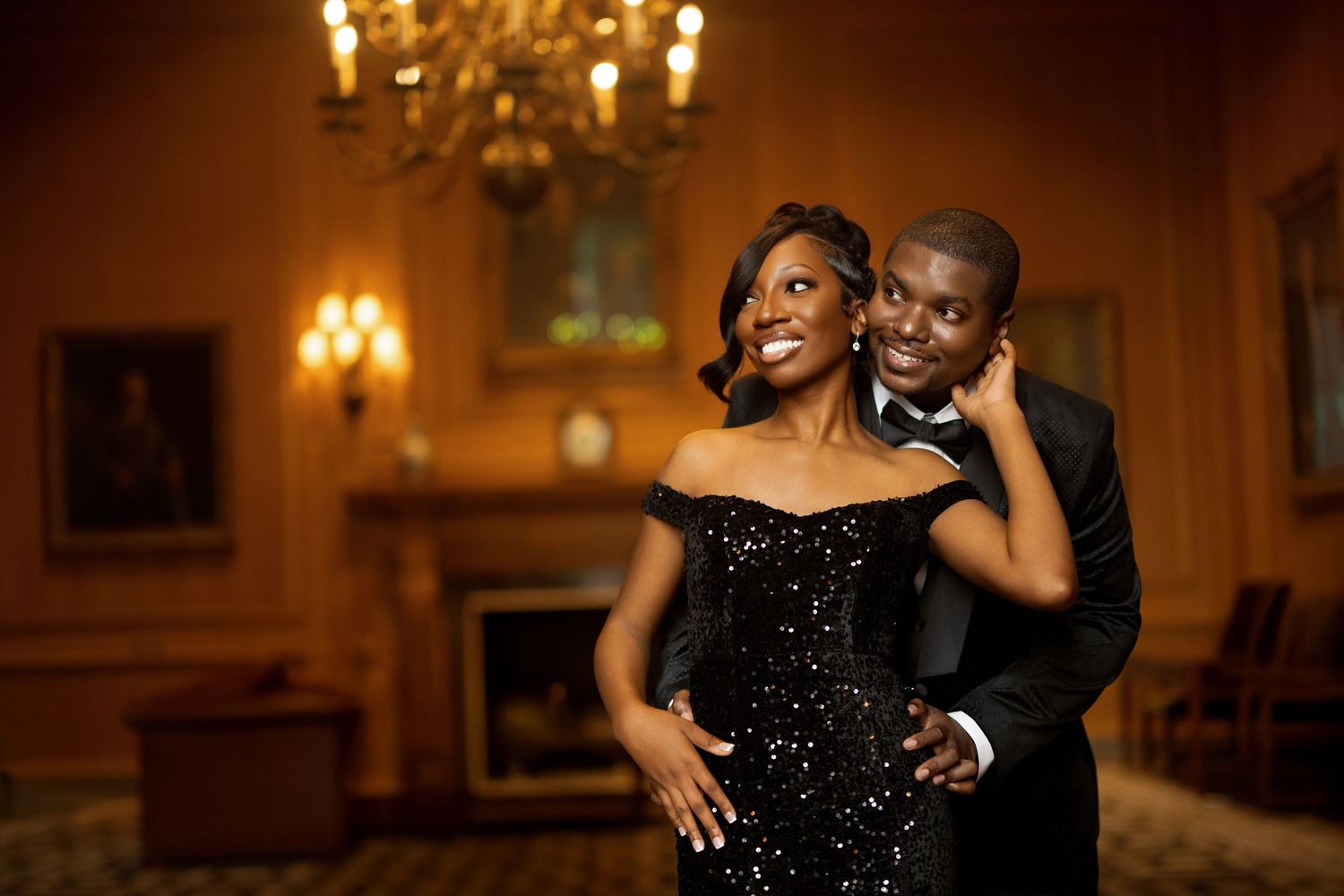 A couple shares a romantic moment in an elegant ballroom with warm lighting and a sparkling black evening gown.