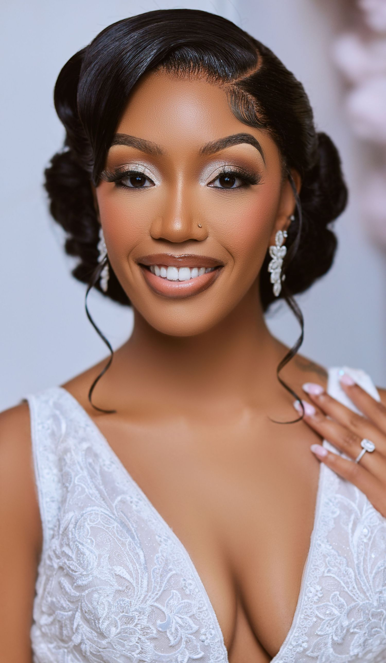 A bride wearing an elegant white lace wedding dress with delicate earrings and glamorous makeup poses for portraits.