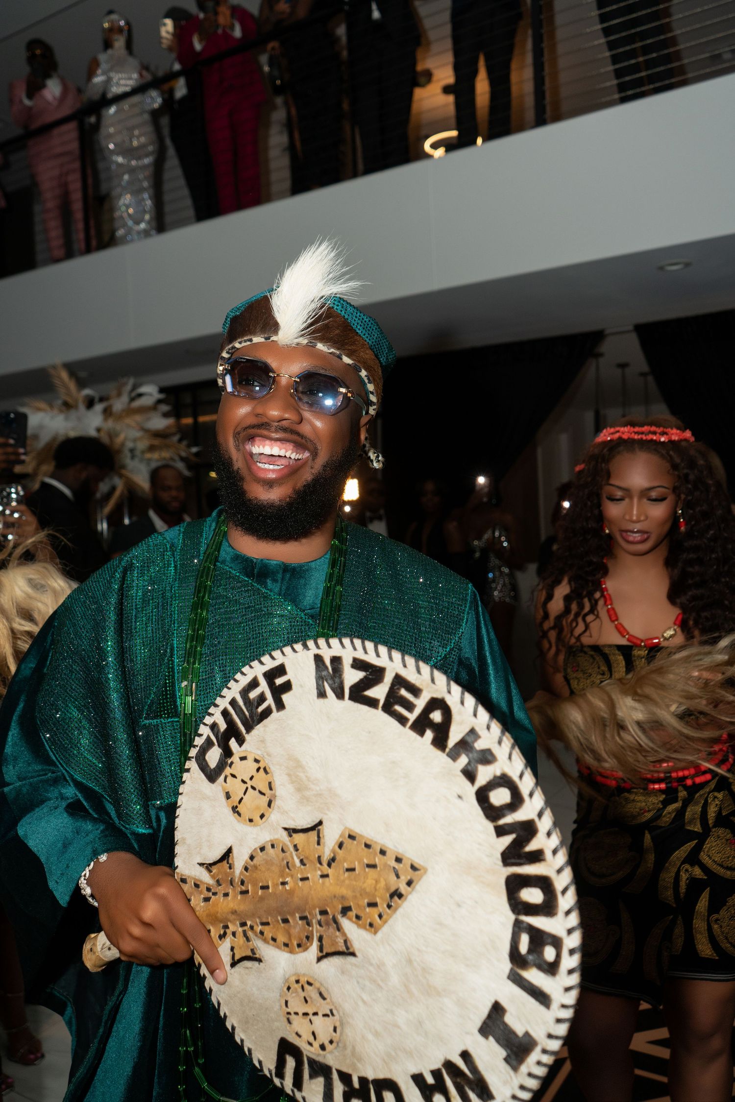 A group of performers in green outfits hold large decorative drums during a cultural celebration event.