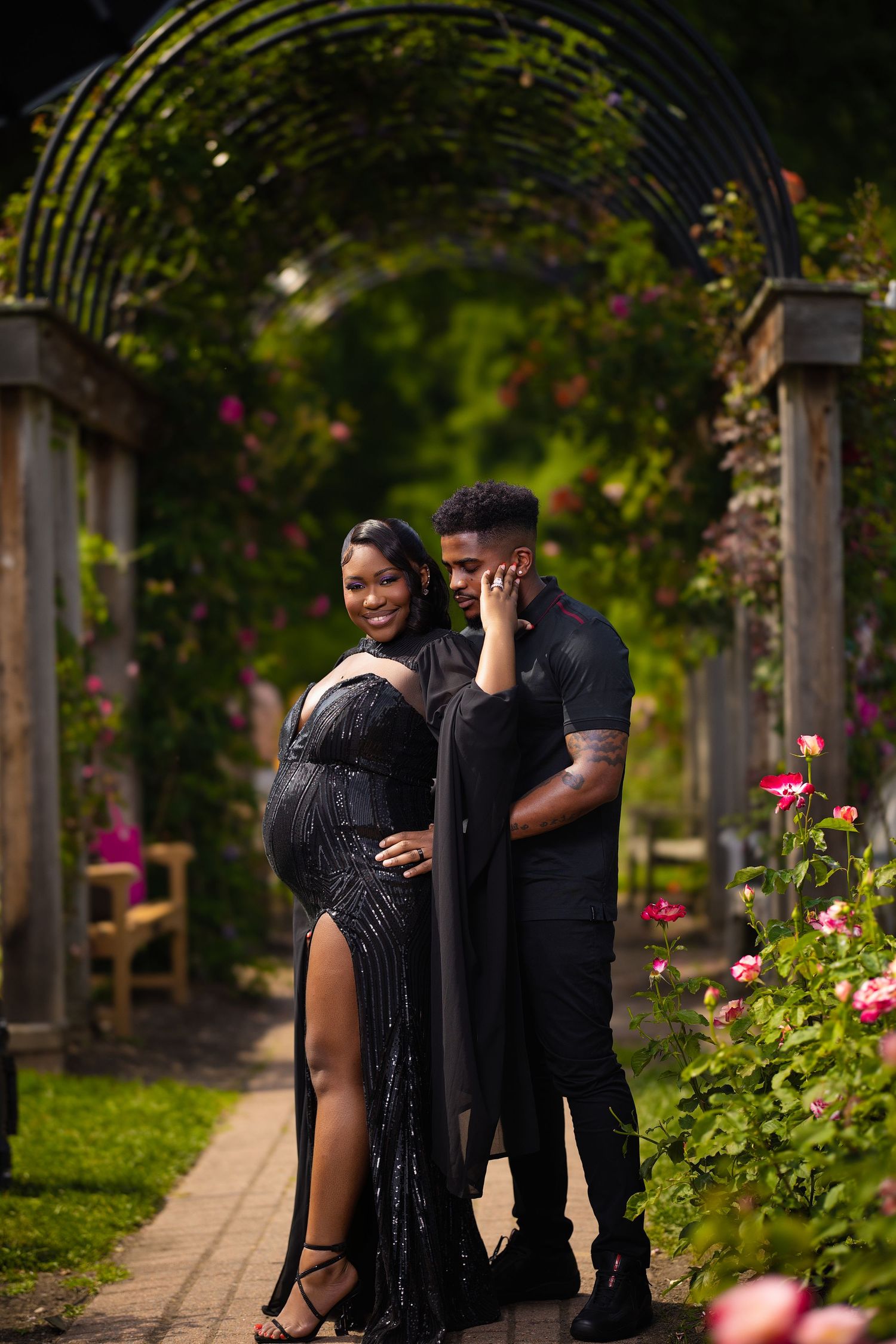 A couple shares an intimate moment together in a garden pathway lined with blooming flowers and greenery.