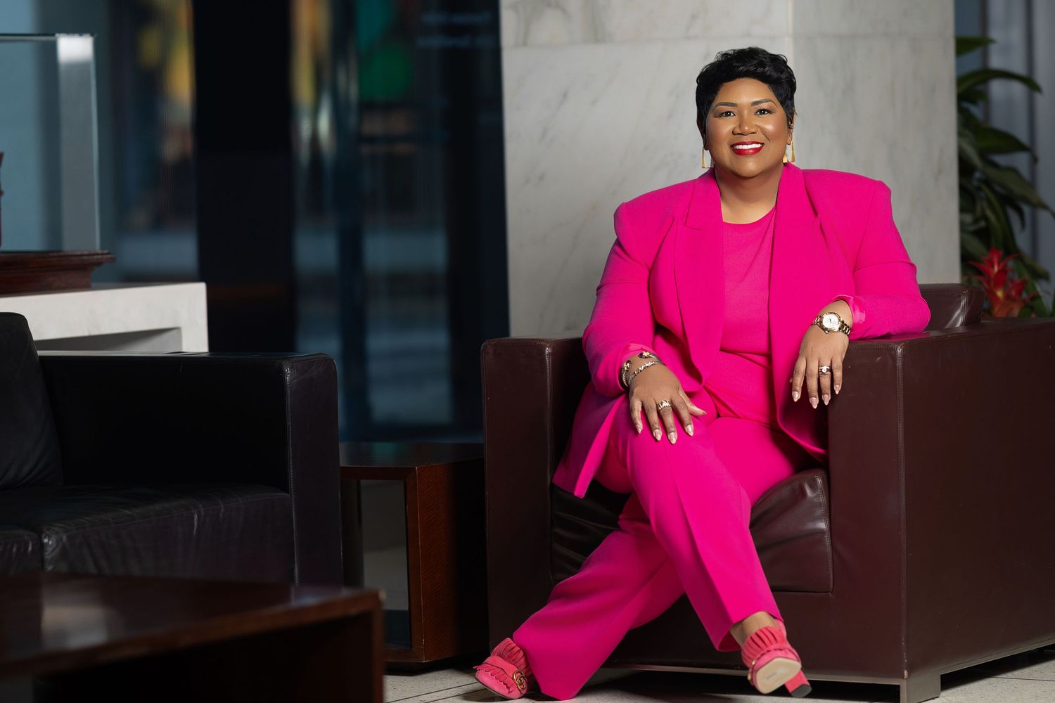 A person in a bright pink blazer sits at a desk in a professional office setting.