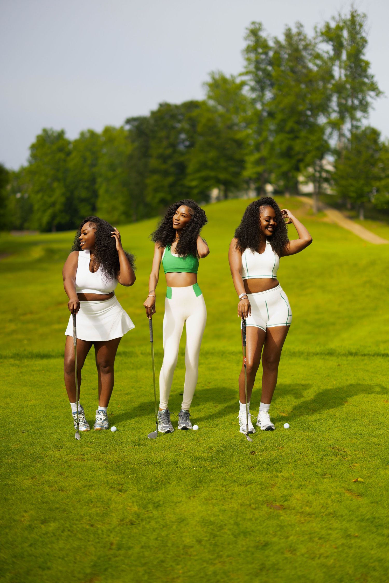Three people in athletic wear pose on a grassy hill during an outdoor photoshoot.