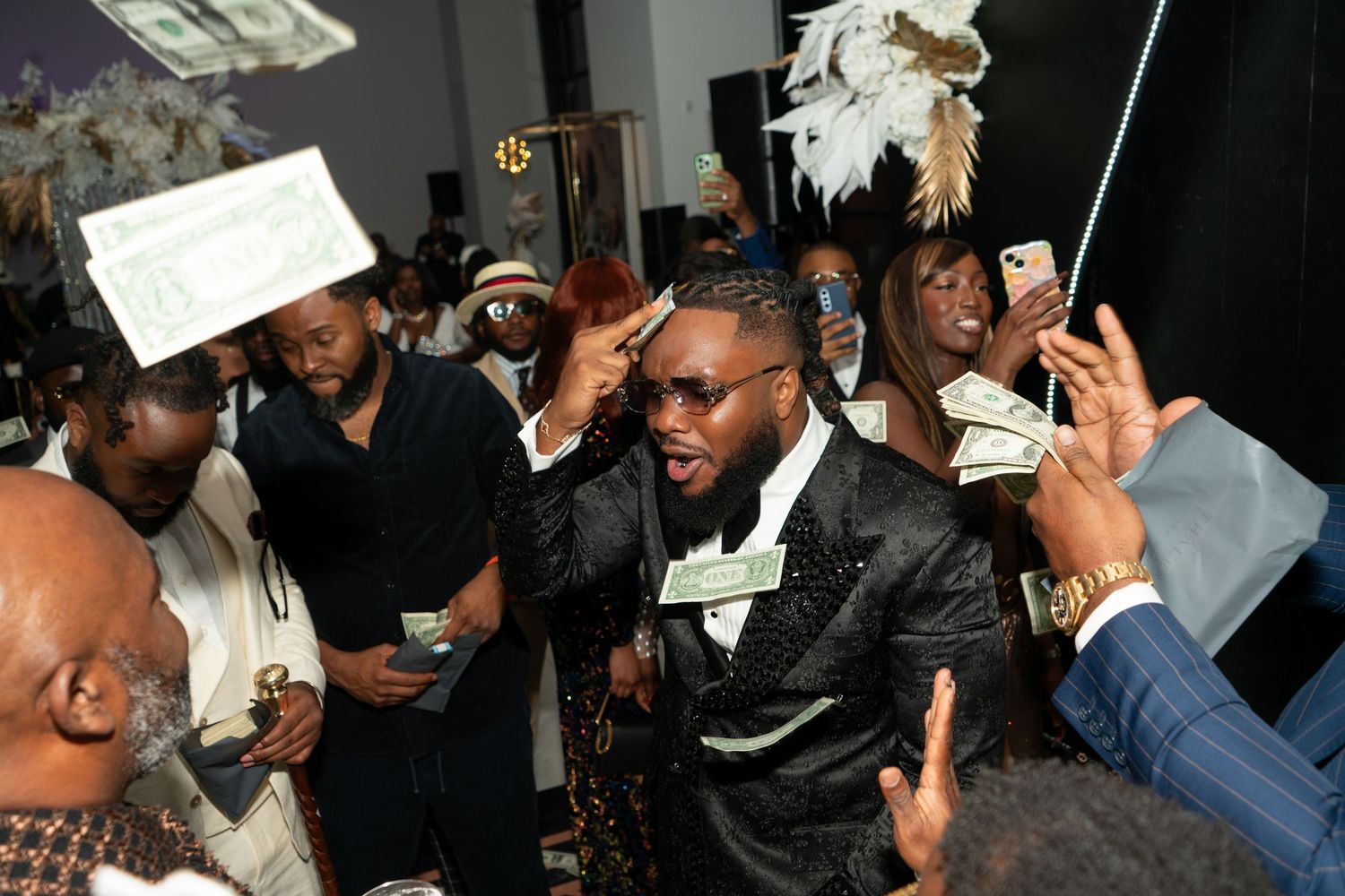 Money falling through the air as people reach up to grab the floating cash in a dark nightclub setting.