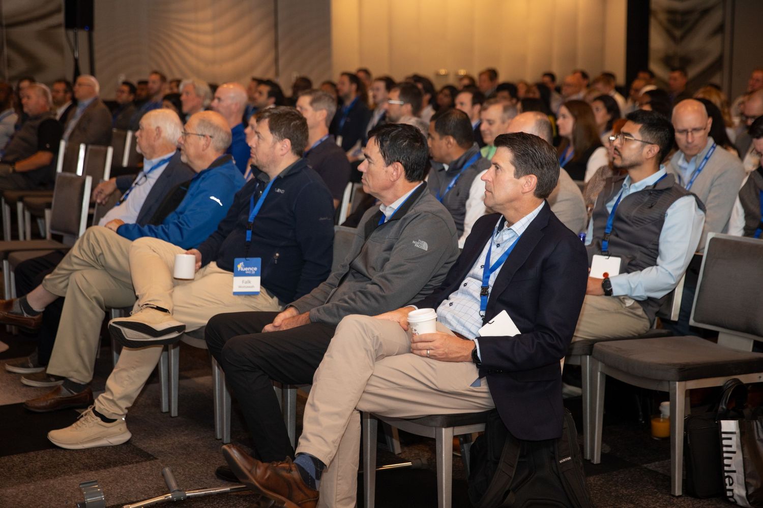 Business conference attendees sitting in rows of chairs listen attentively to a presentation in a corporate venue.