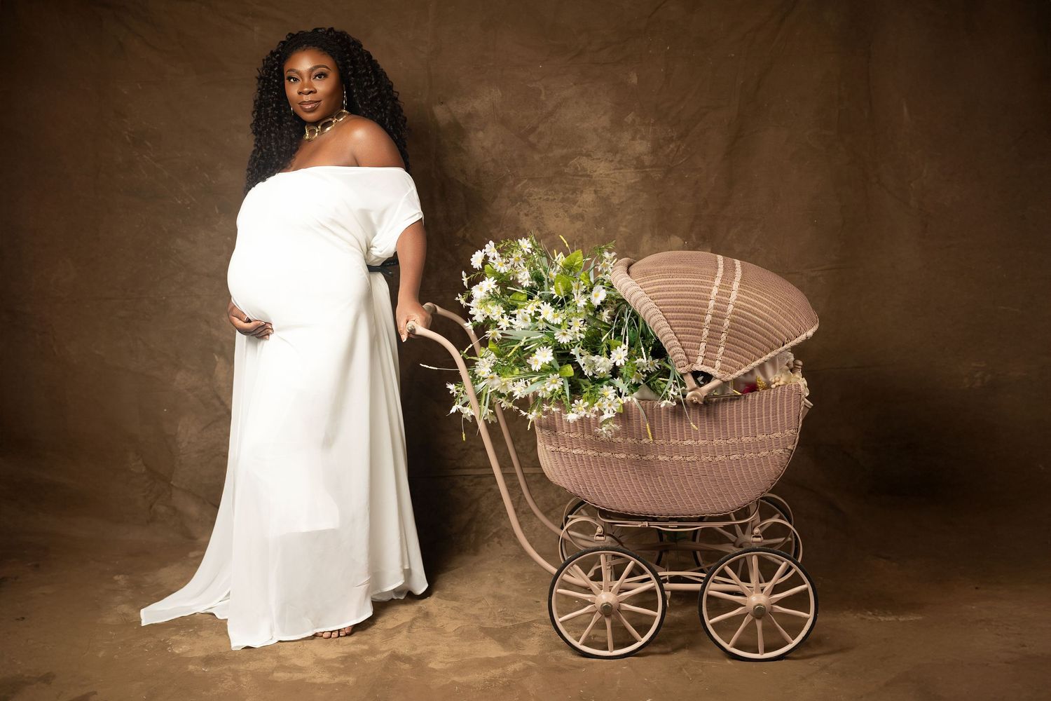 Vintage-style maternity photo series with brown backdrop and antique baby carriage featuring white floral accents.