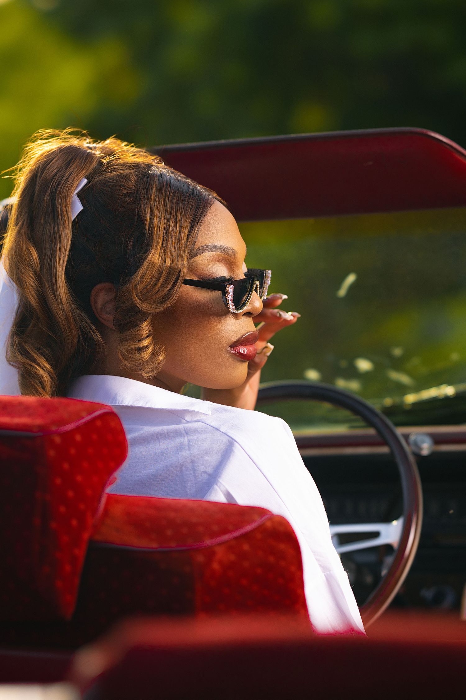 Person relaxing in red vintage convertible car with sunglasses on sunny day.