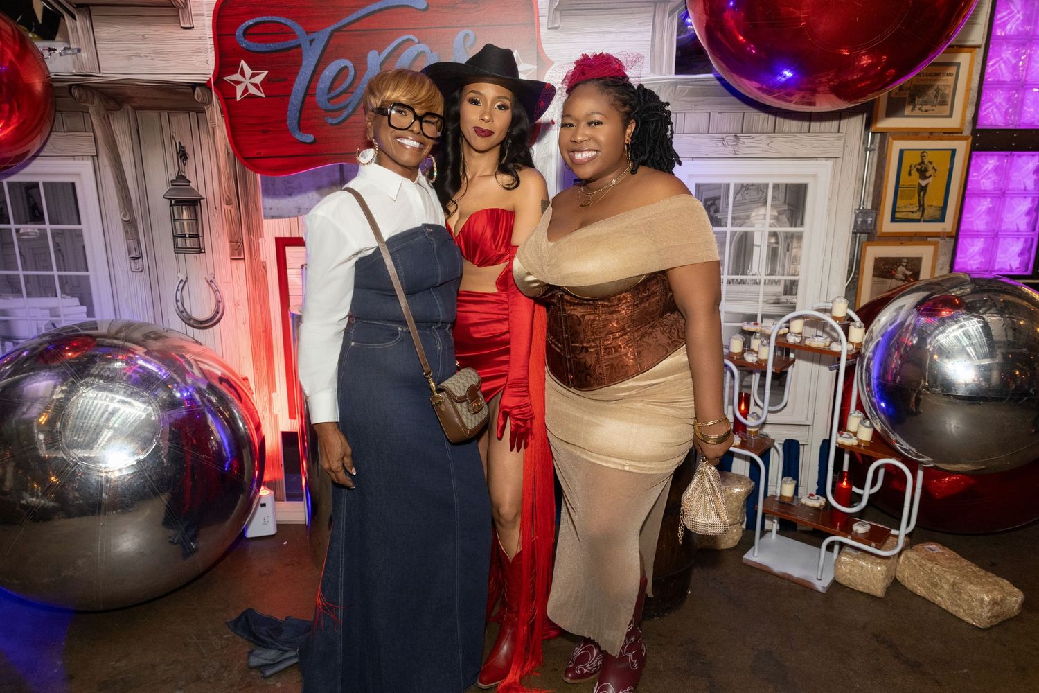 Three people pose together at a festive party with silver disco balls and neon lighting in the background.