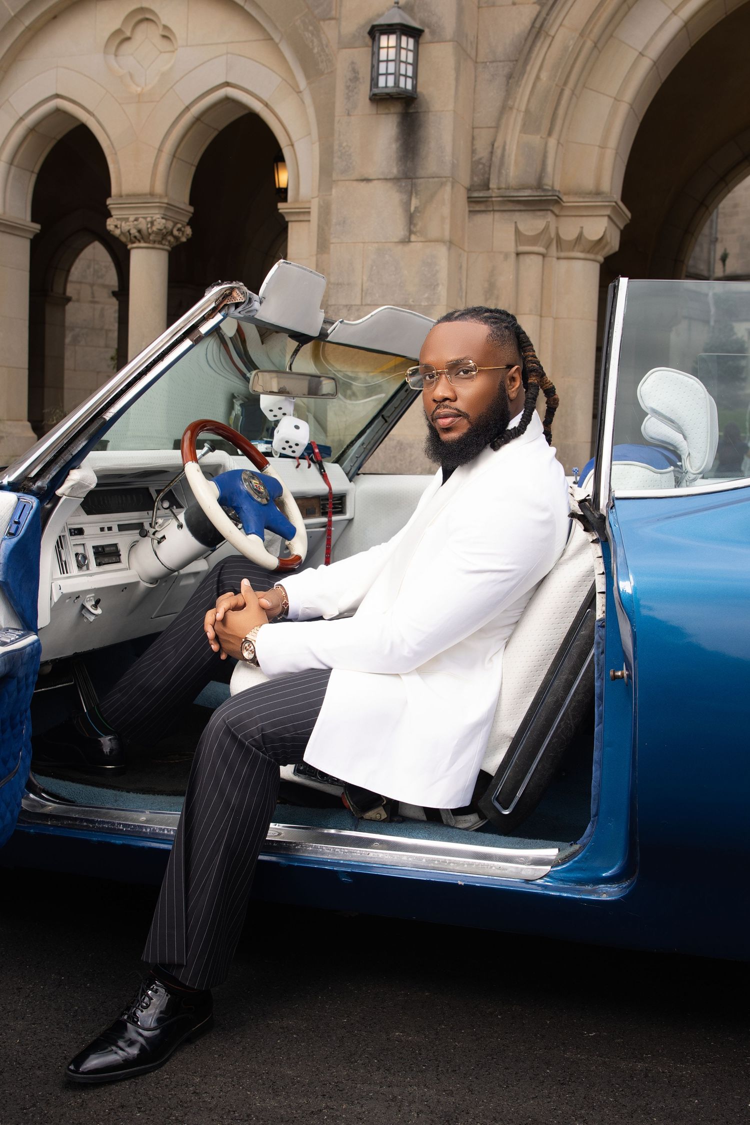 Luxury fashion series posed in and around a classic blue convertible car under stone archways.