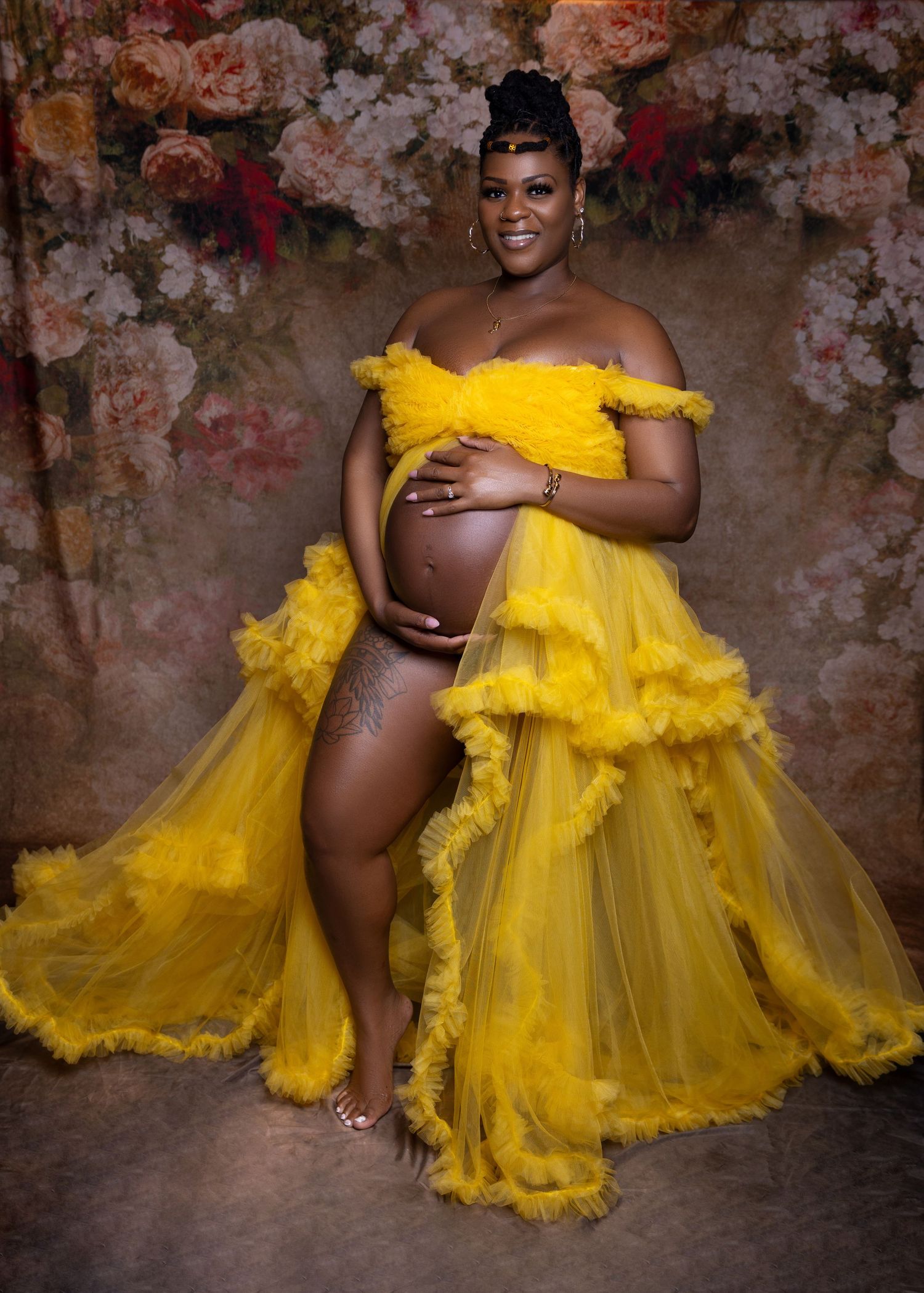Artistic maternity photo series showing figure in flowing yellow tulle gown against textured dark backdrop.