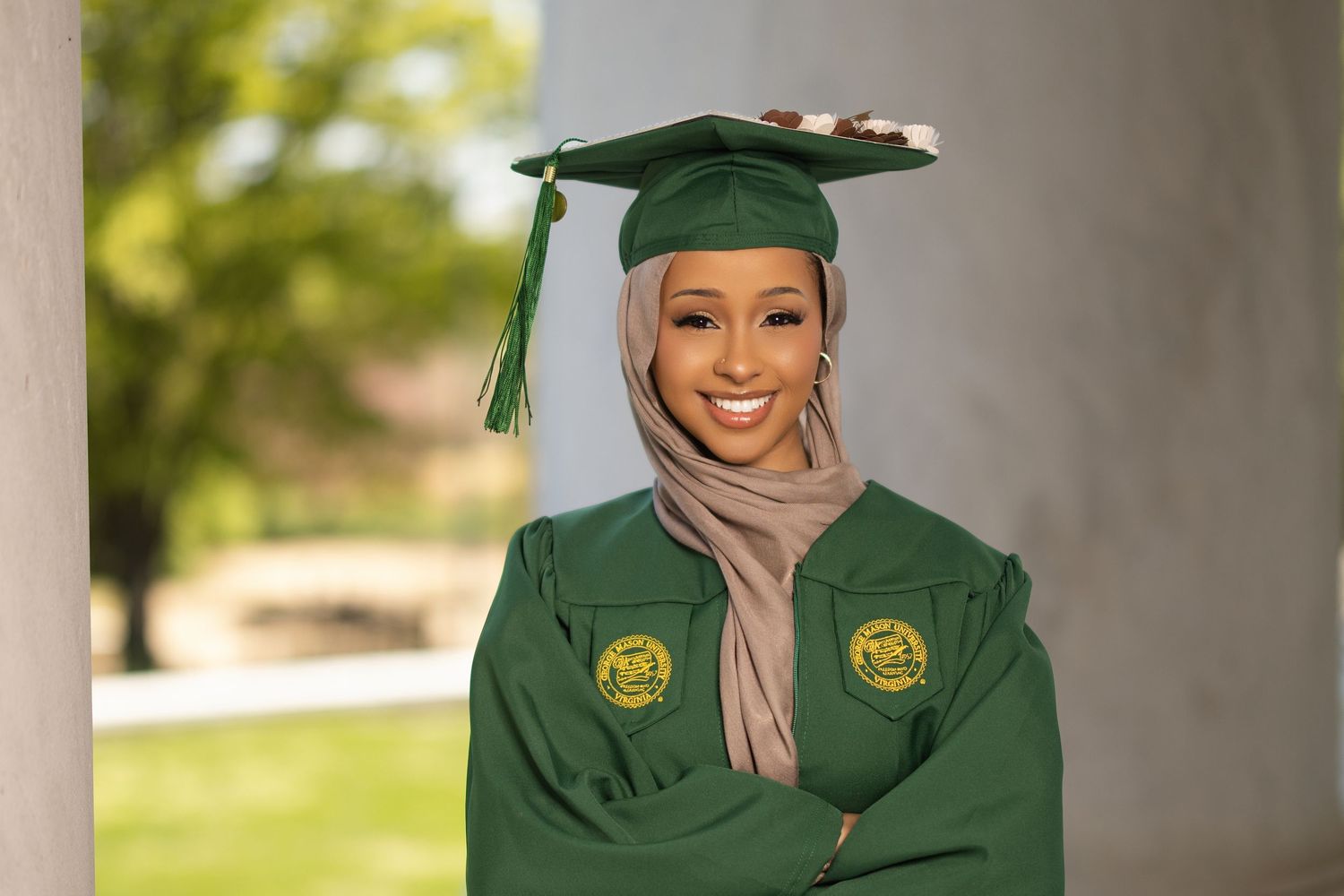 Graduate in green cap and gown poses for celebratory graduation photos outdoors on a sunny day.