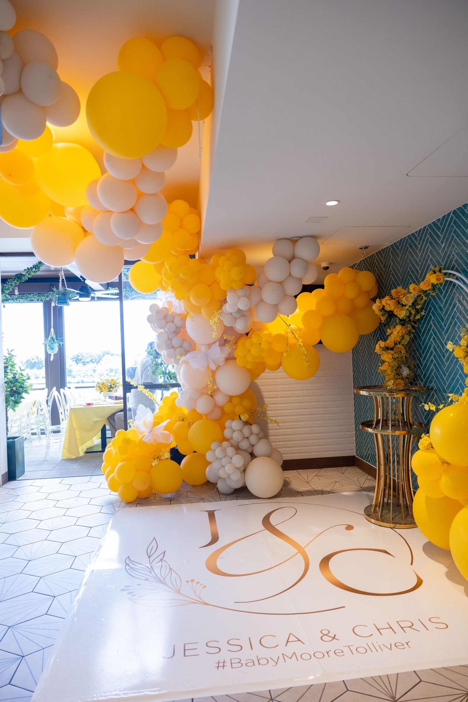 Yellow and white balloon arch installation with monogram text for Jessica and Chris on white floor.
