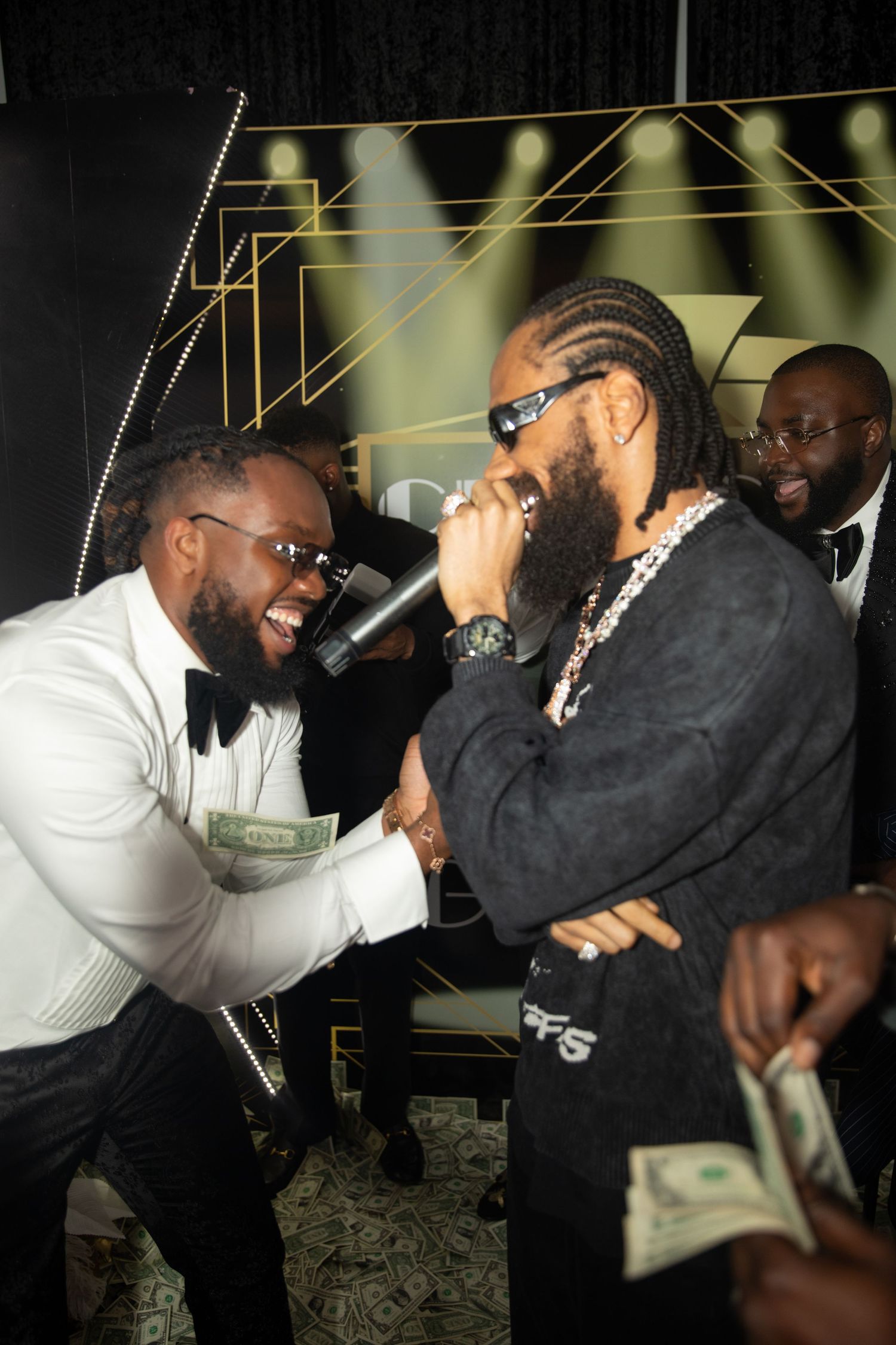 Two men in black and white attire share a joyful moment laughing together at a nighttime event.