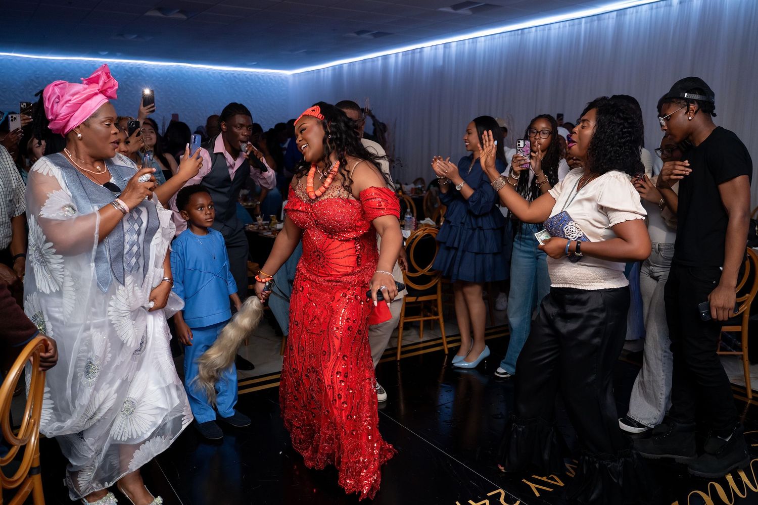 People dancing and celebrating on a dimly lit dance floor with blue LED lighting along the ceiling.