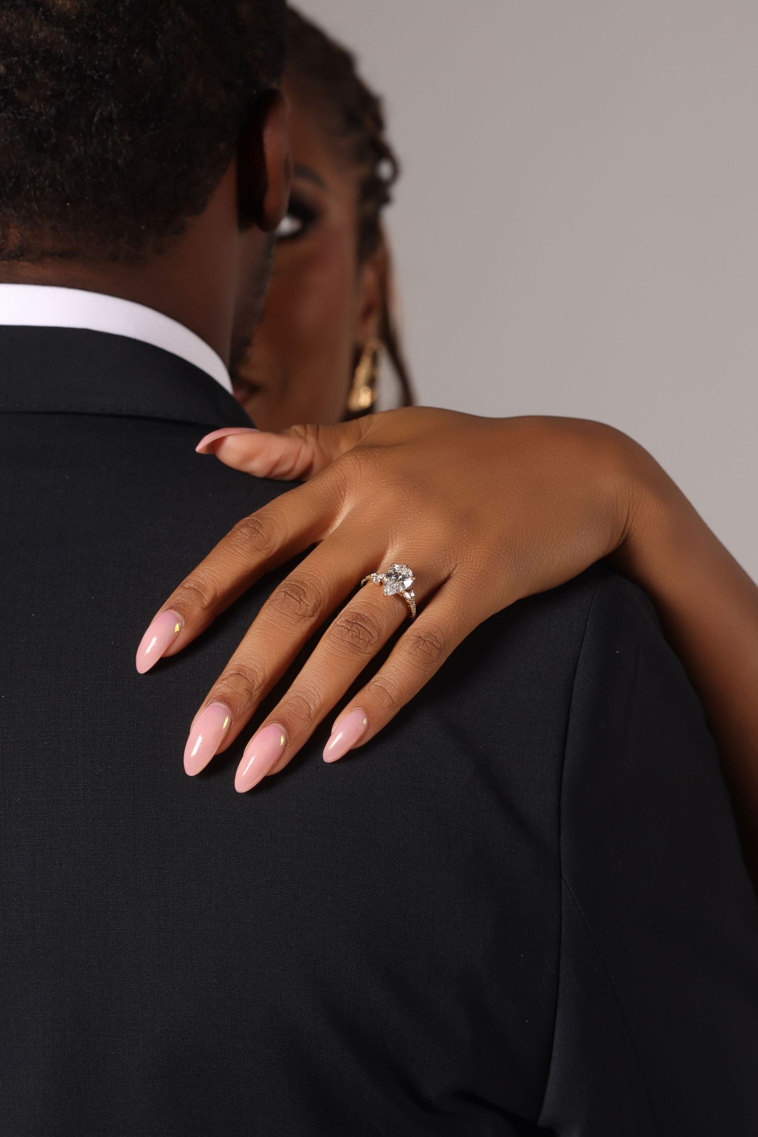 Close-up of hands with engagement ring resting on black suit jacket.