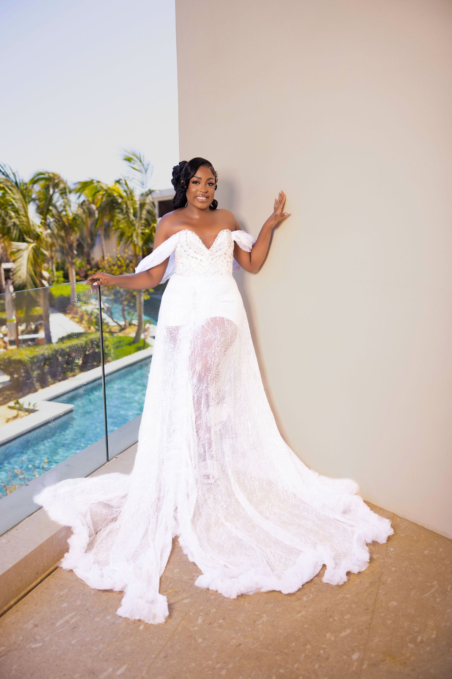 A person in a flowing white wedding dress poses dramatically by a poolside at a tropical resort.