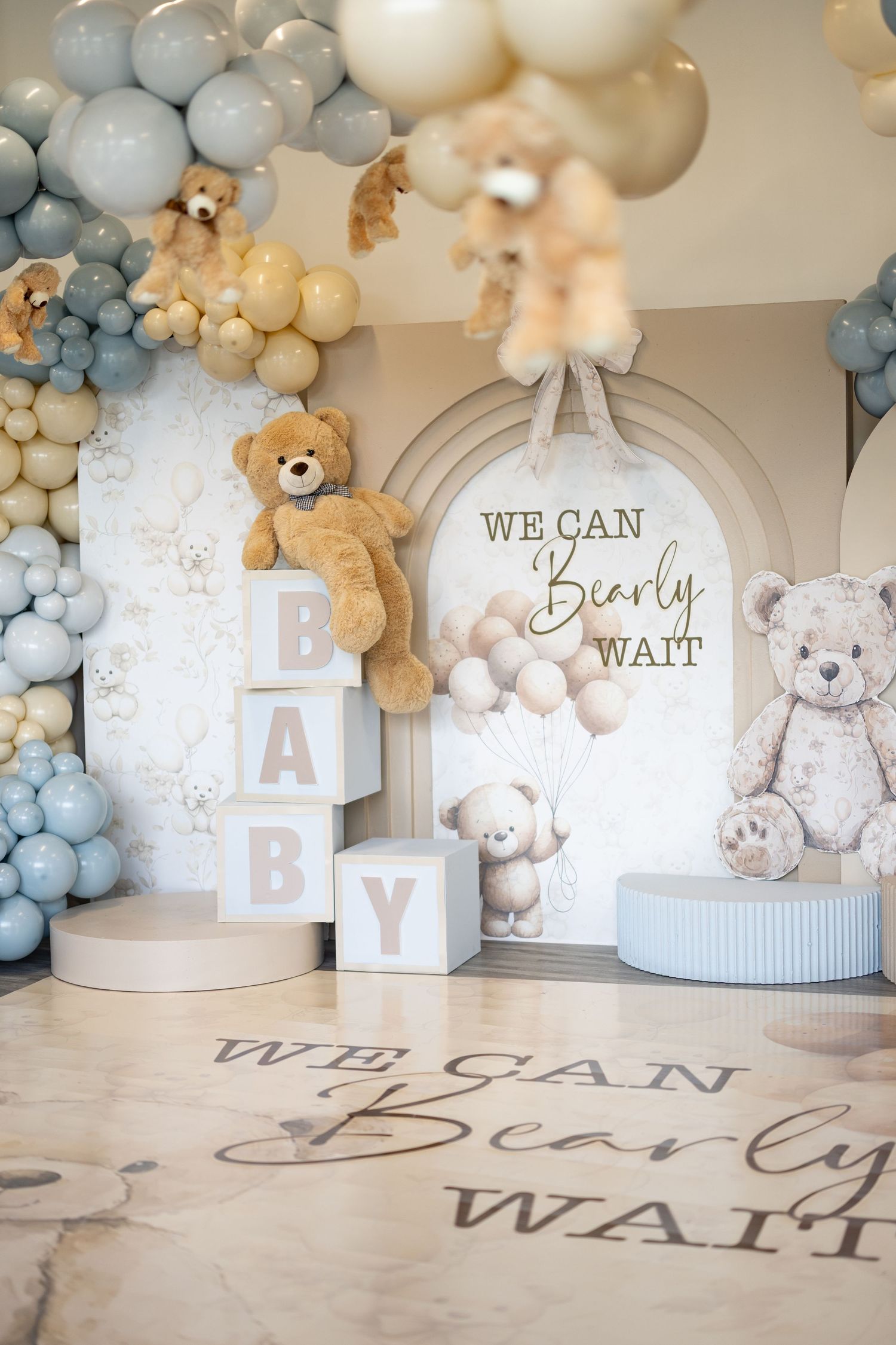 Baby shower decoration setup with blue balloons, teddy bears, and 'We Can Bearly Wait' signage.