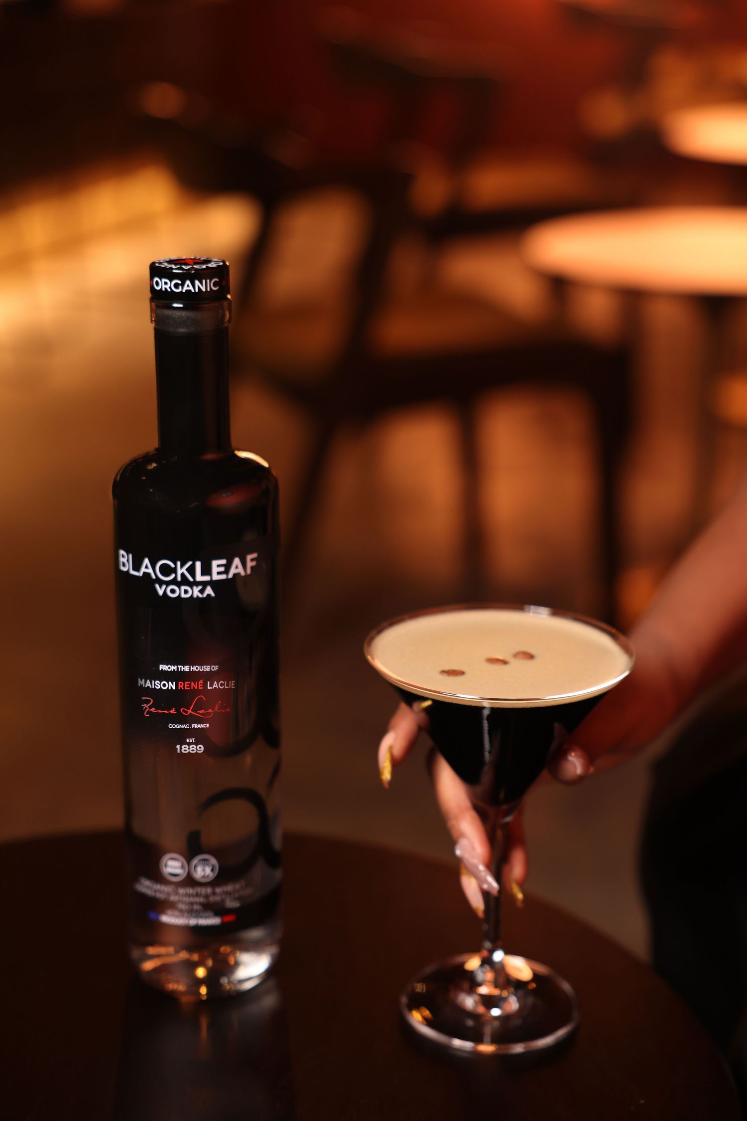 Black Leaf vodka bottle and cocktail glass on dark table with ambient lighting.