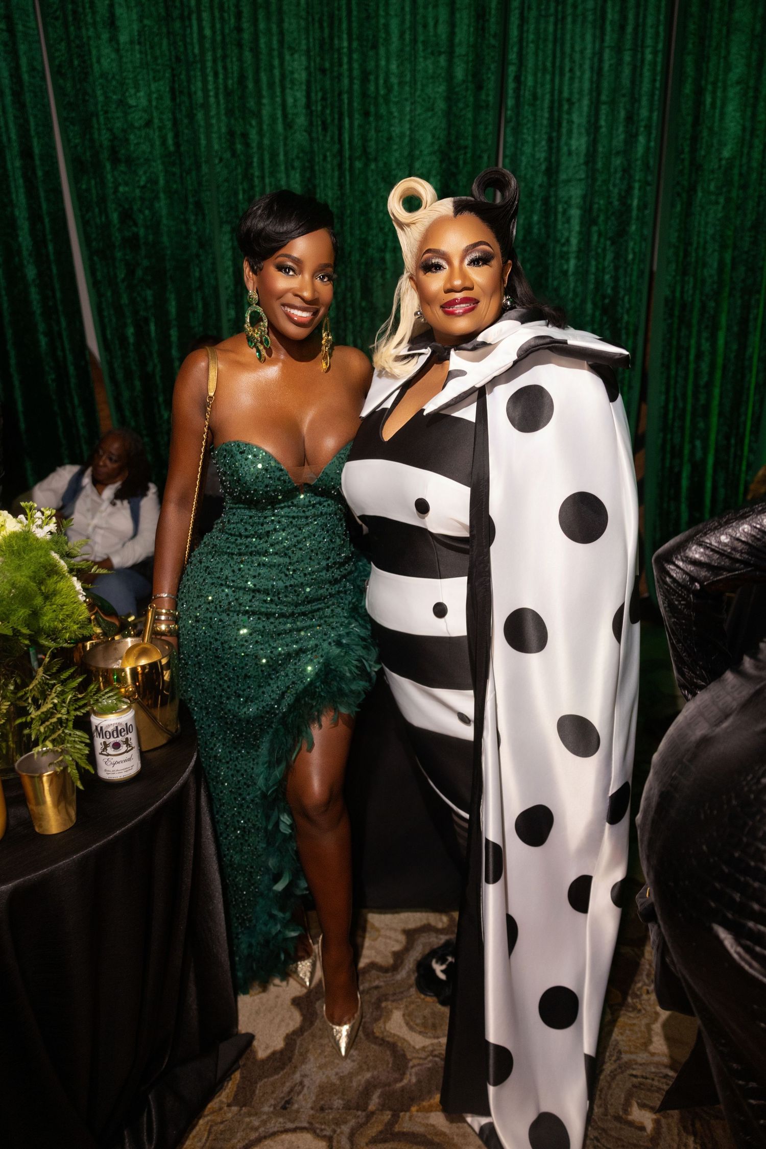 Elegant evening event with emerald dress and dramatic black and white costume against green backdrop.