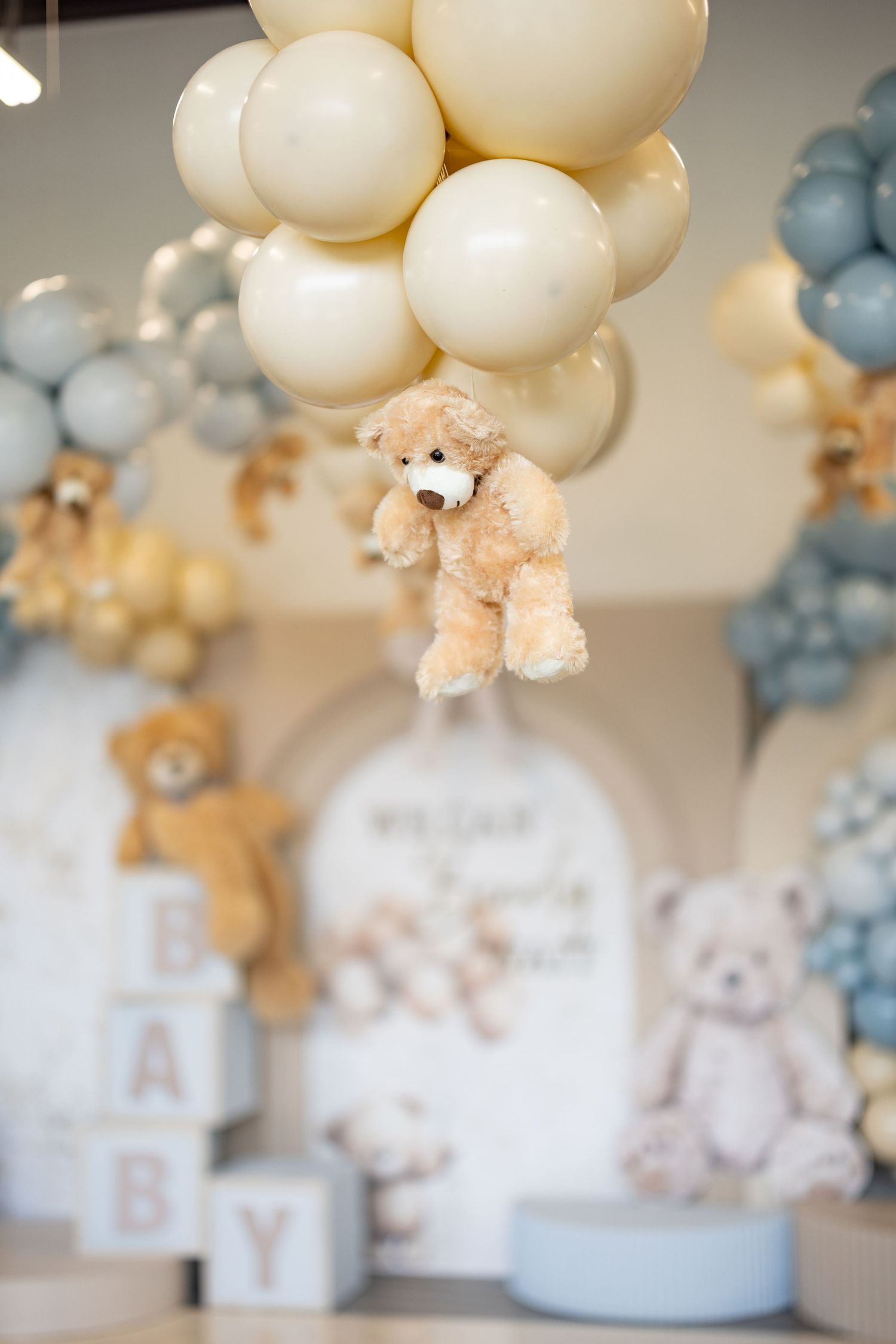 Cream and blue balloon arch with teddy bear accents for baby shower celebration.
