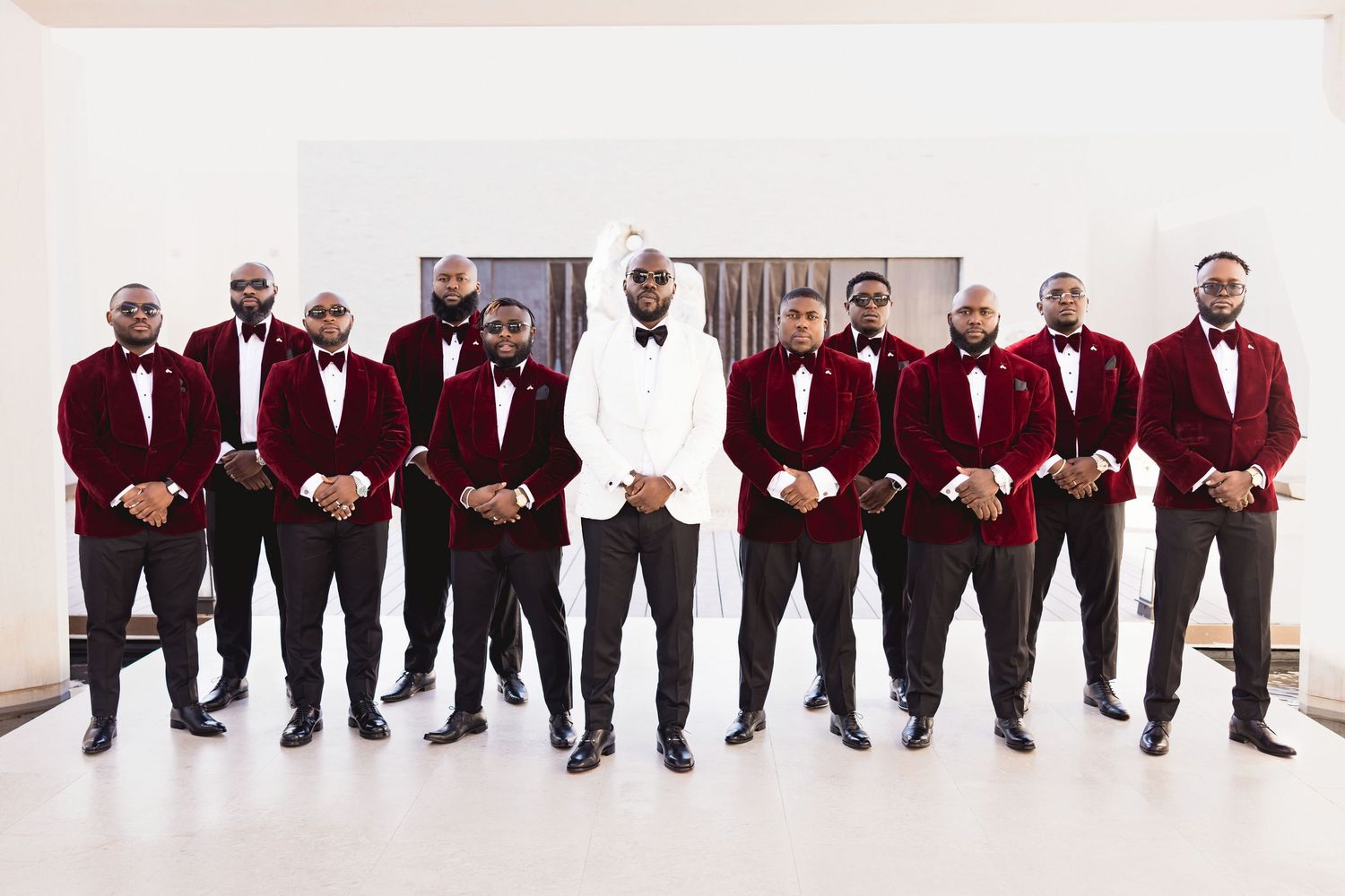 Wedding party members in burgundy suits sit in a row showing off their colorful socks and dress shoes.