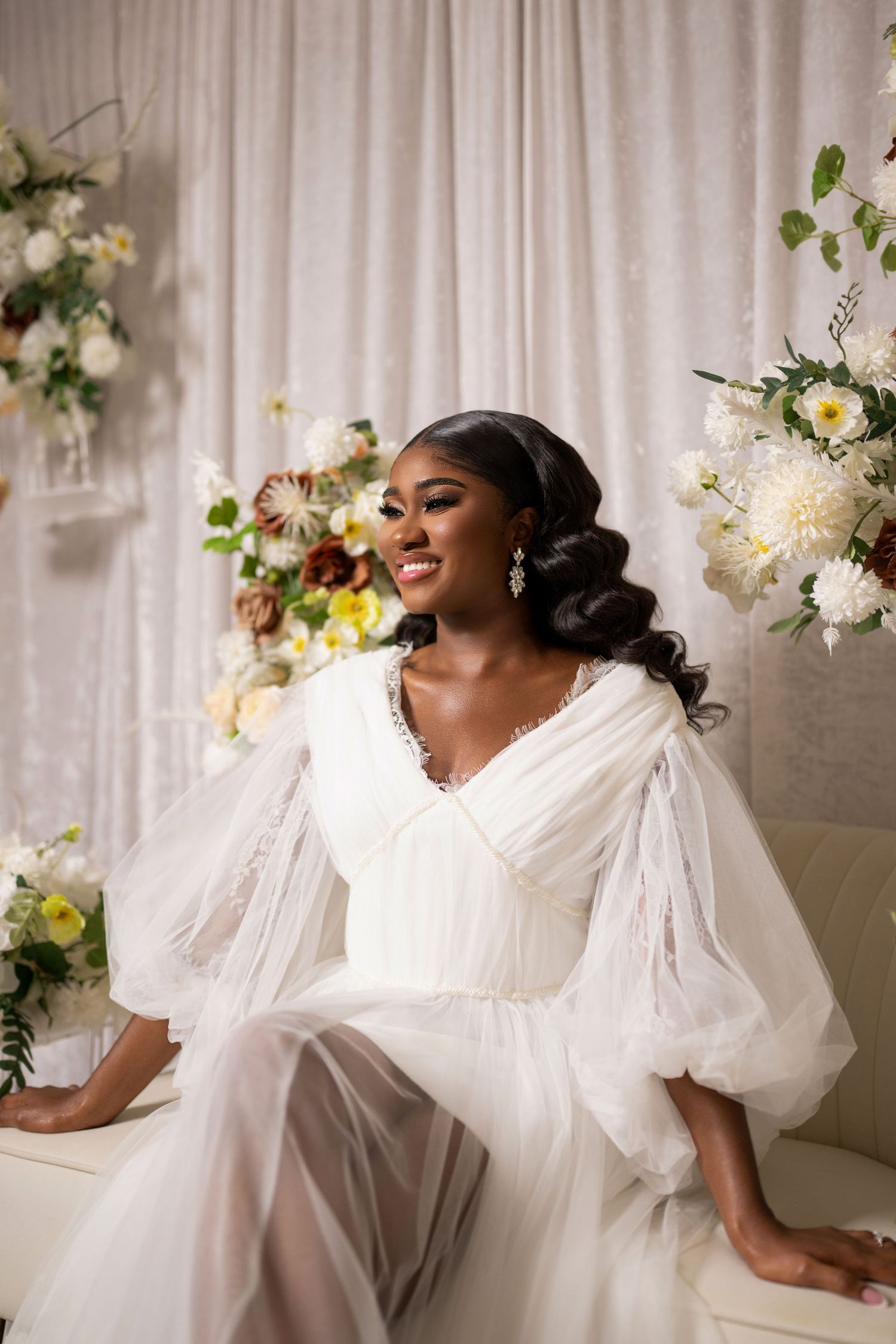 Elegant bridal portrait with white puffy sleeve dress surrounded by floral arrangements.
