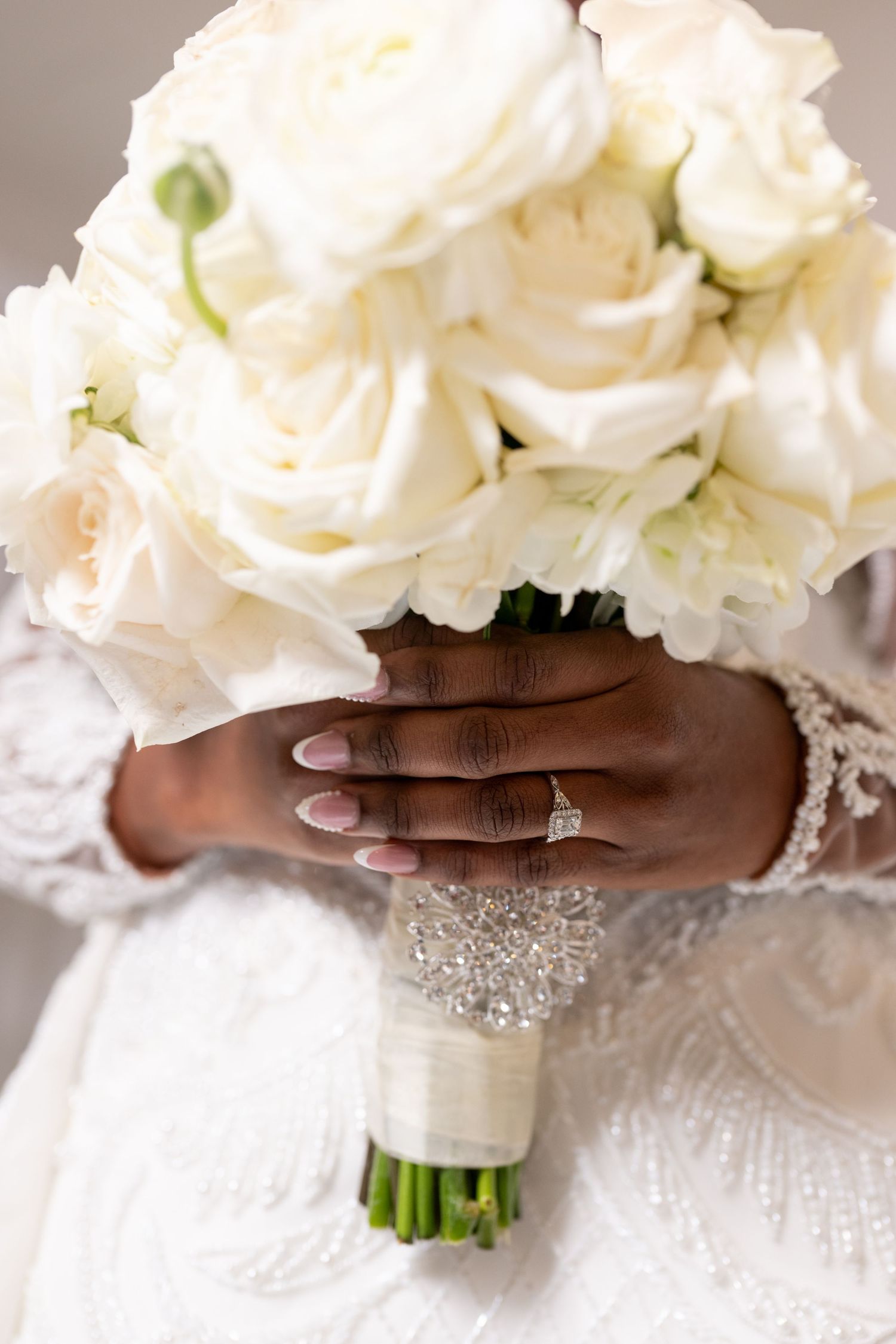 Close up of bridal bouquet with white roses held by hands wearing lace and engagement ring.