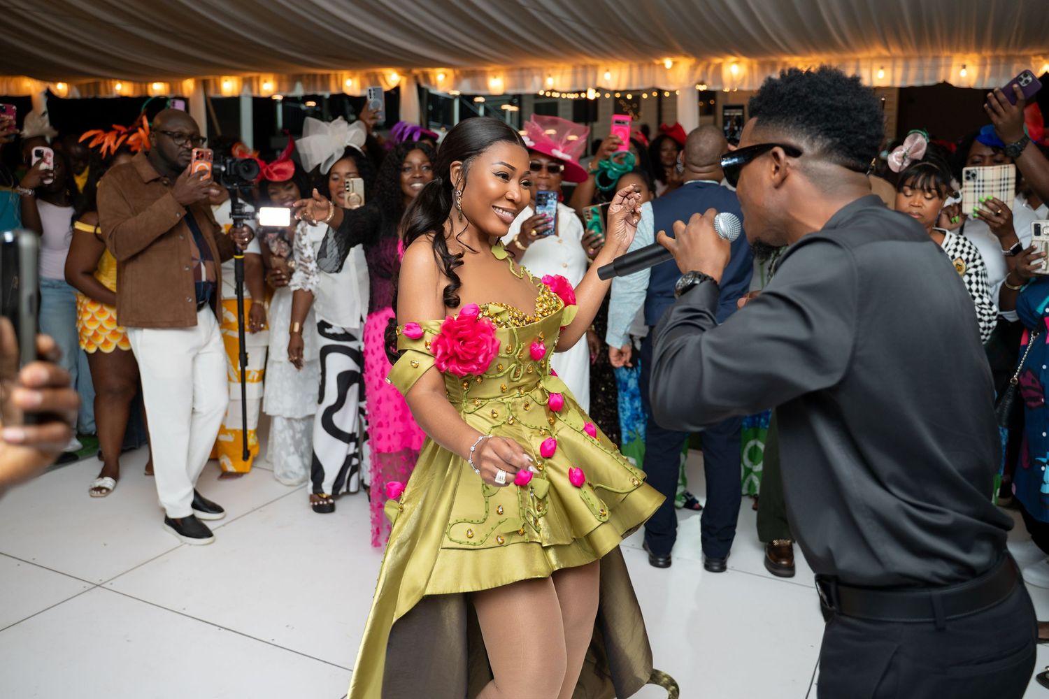 A festive wedding reception dance floor with guests dancing under a white tent canopy.