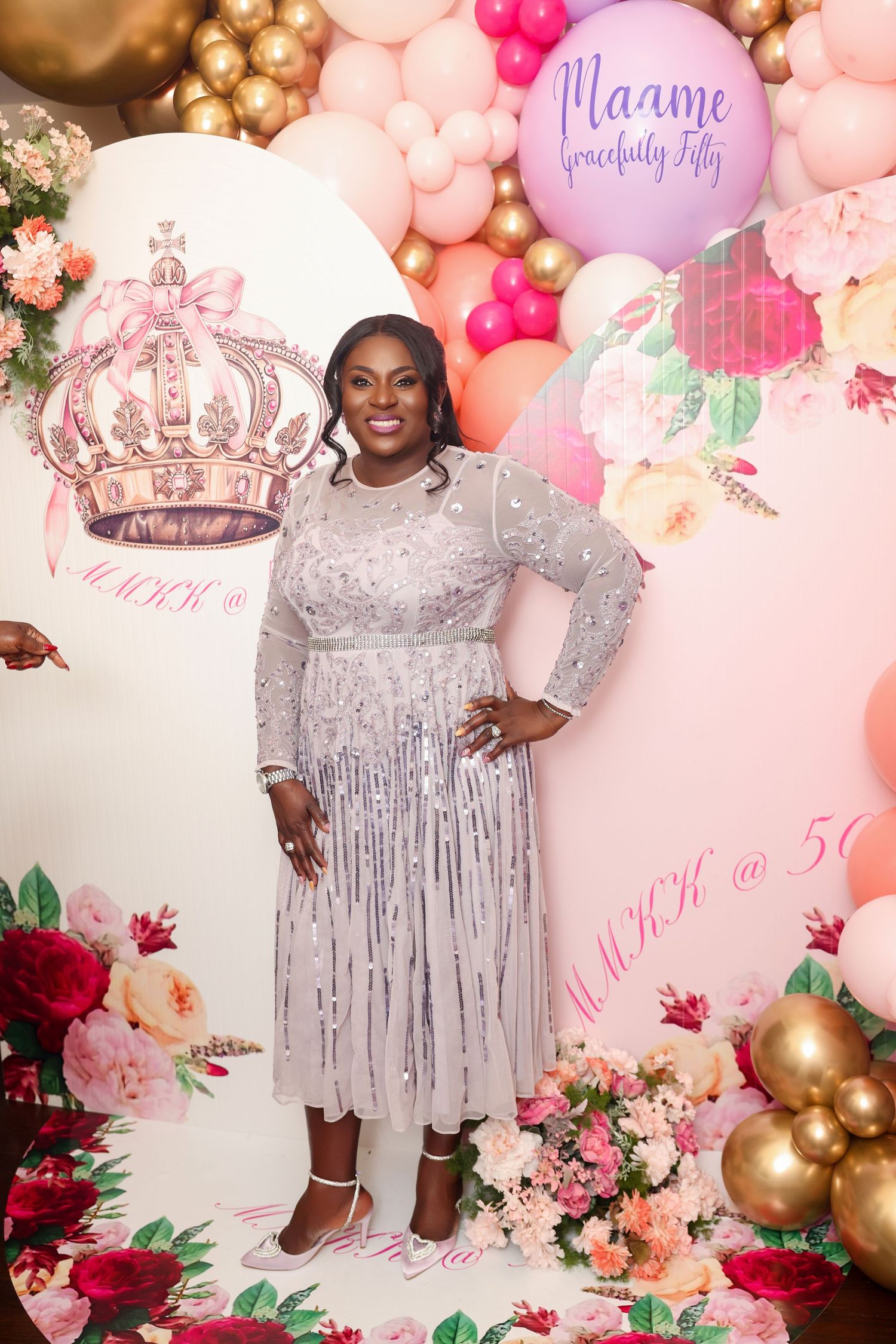 Sparkly silver sequin party dress against pink balloon arch and floral backdrop at celebration event.