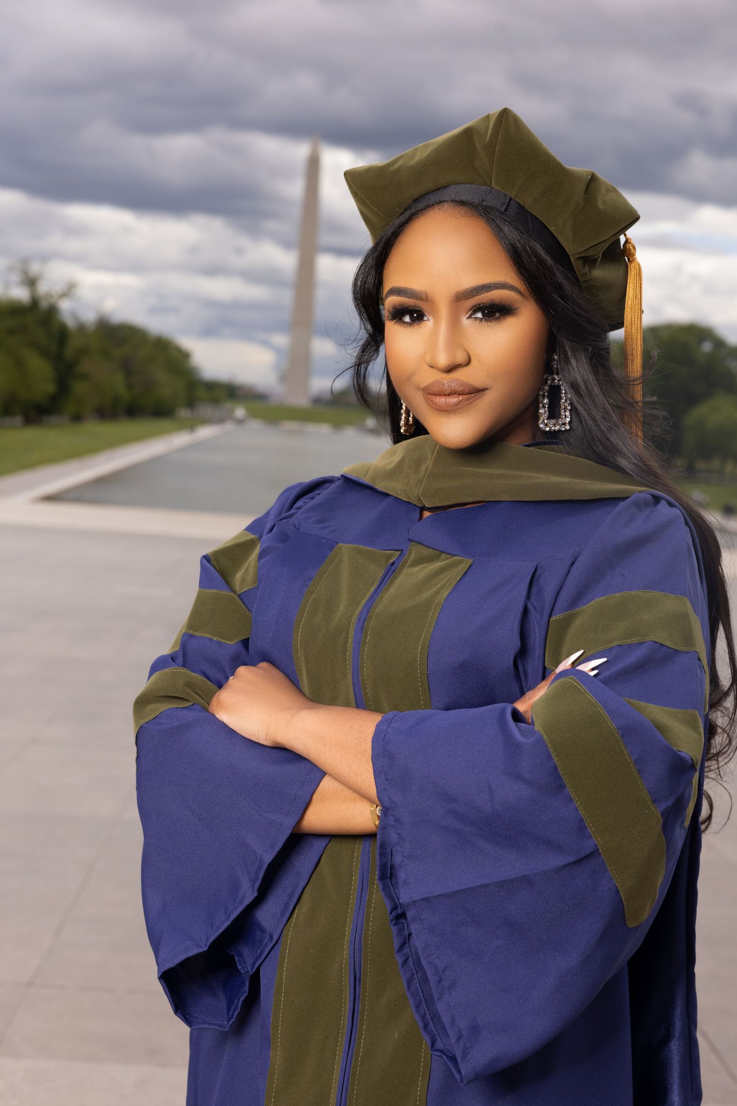 Graduate wearing navy blue and olive green academic regalia poses for graduation photos outdoors.