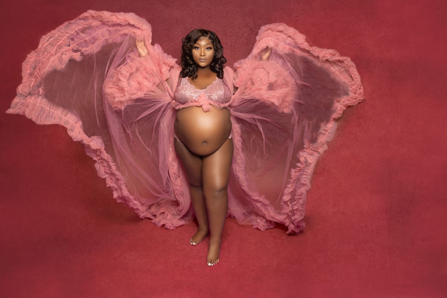 Sensual boudoir photo of woman in pink tulle fabric against burgundy background creating dreamy romantic mood.